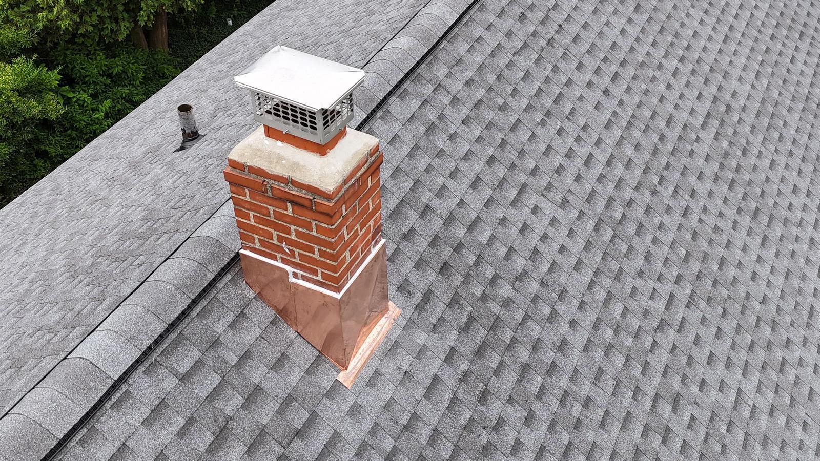 Brick chimney on a gray shingled roof with a metal cap.