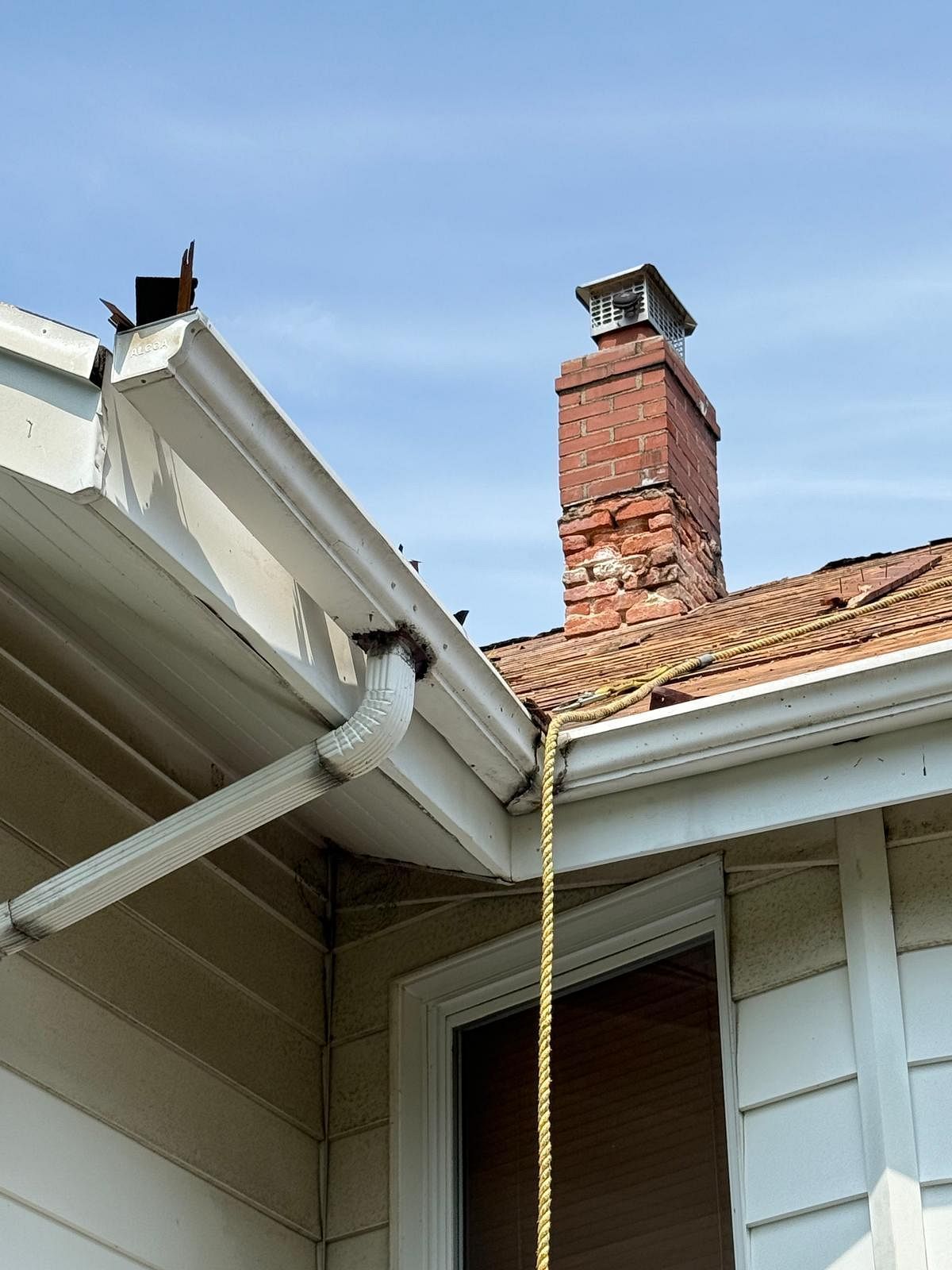 House roof gutter with a yellow rope hanging beside a brick chimney