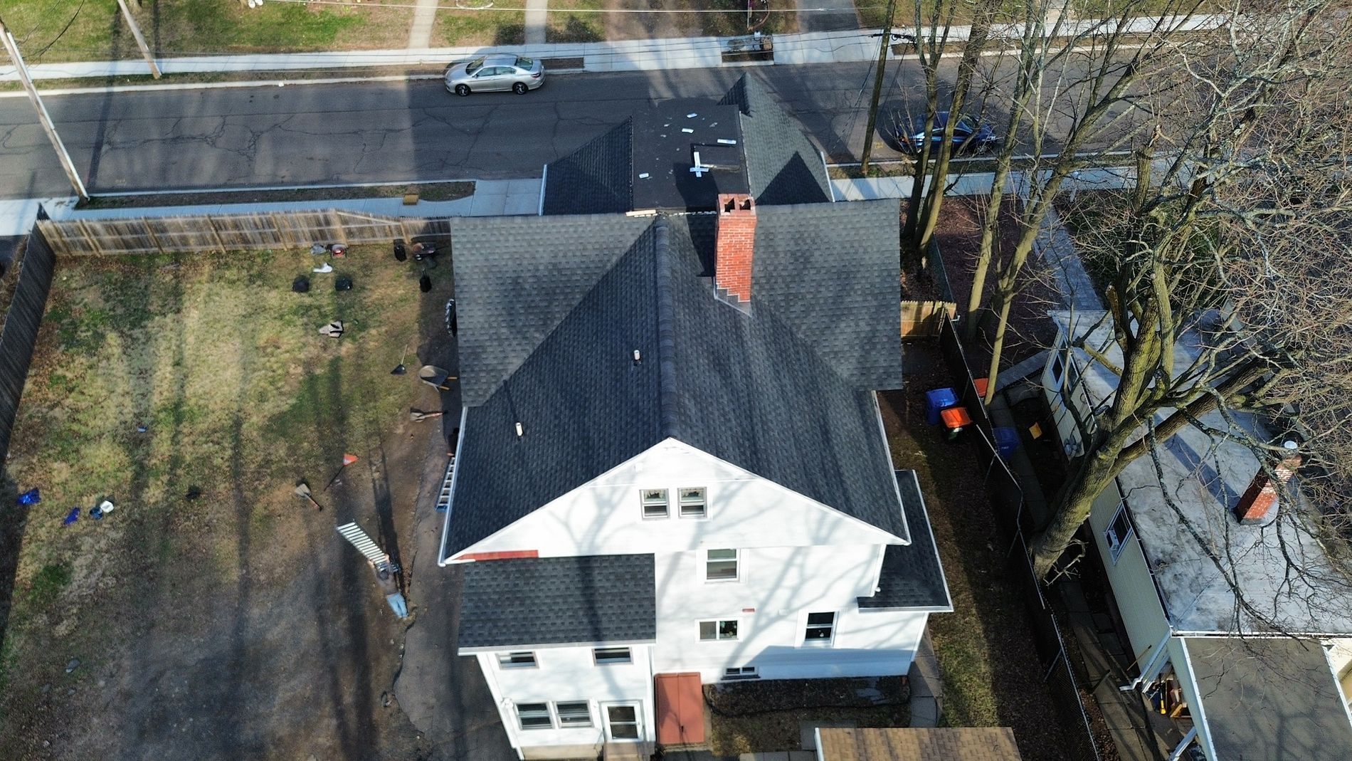 Aerial view of a white house with a dark roof beside a road and trees.