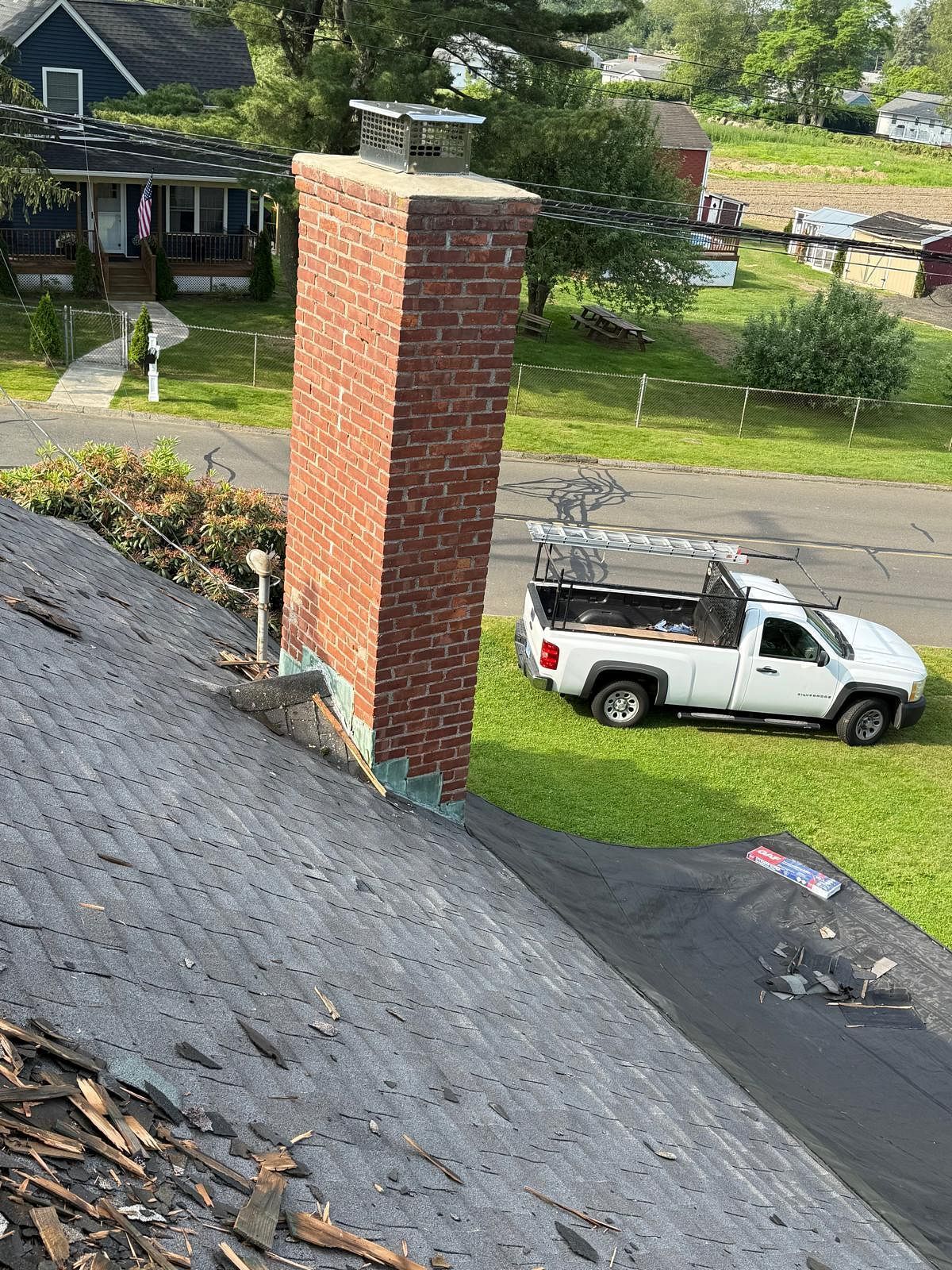 Brick chimney on a dark shingled roof, with a white work truck and green yard below.