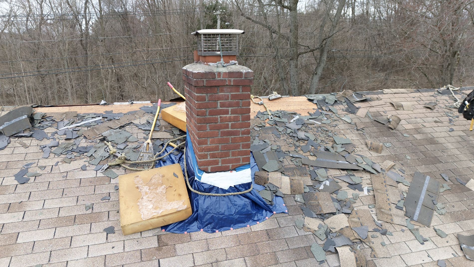 Brick chimney on a damaged roof with blue tarp and debris surrounding it
