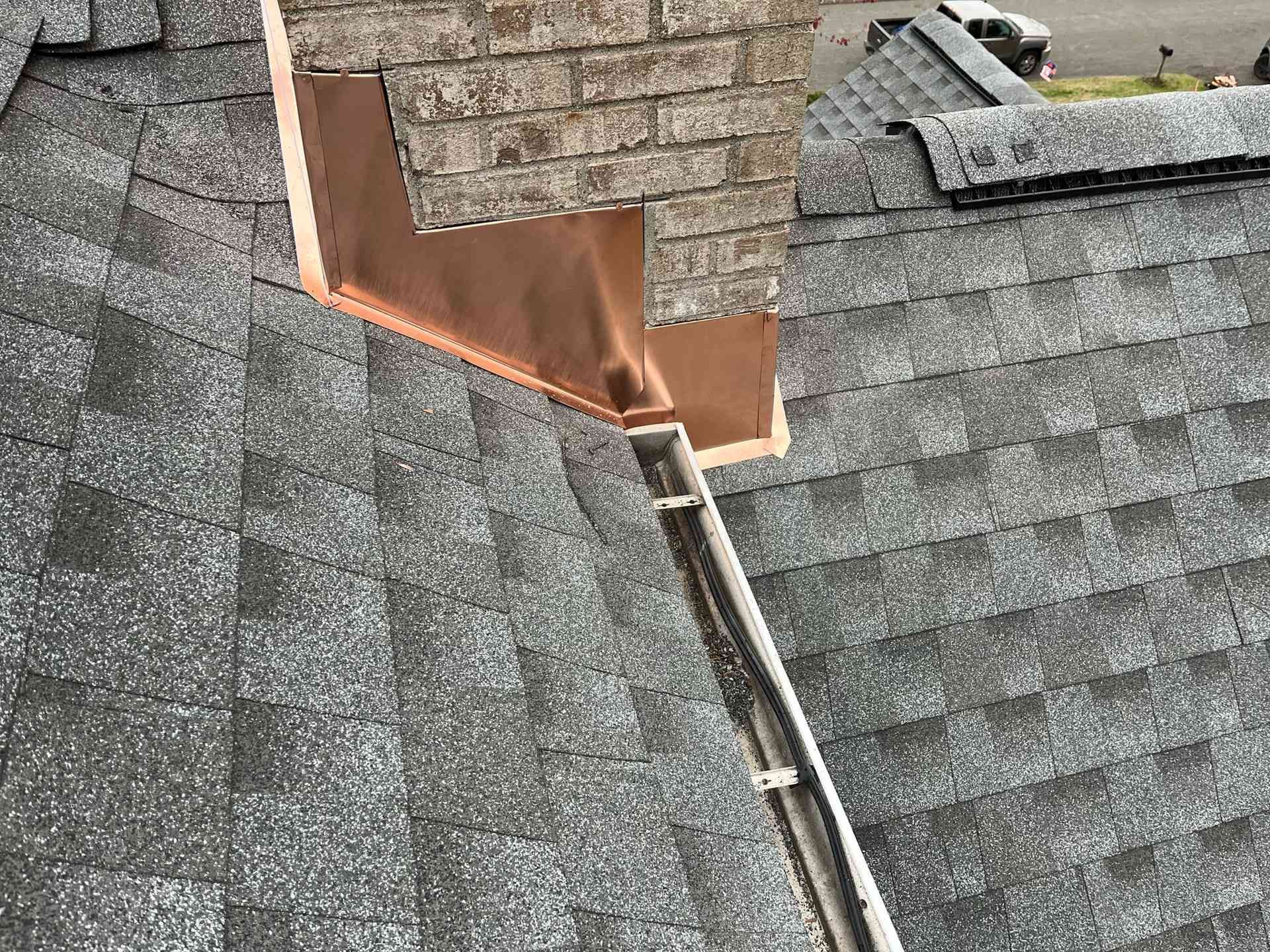 Damaged roof shingles with exposed copper flashing around a vent or chimney opening