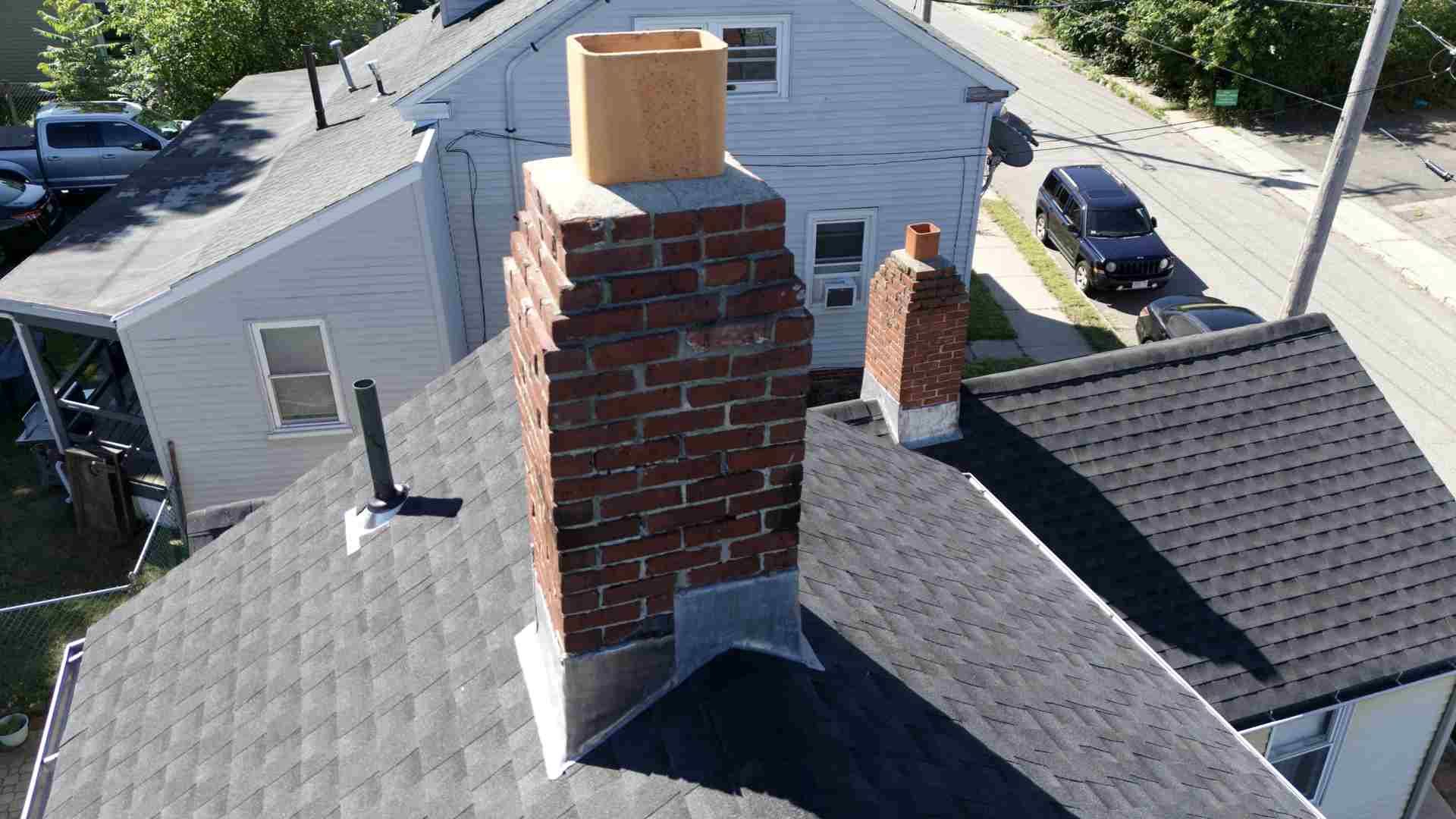 Rooftop view of two brick chimneys on a gray shingled house, with neighboring homes in the background