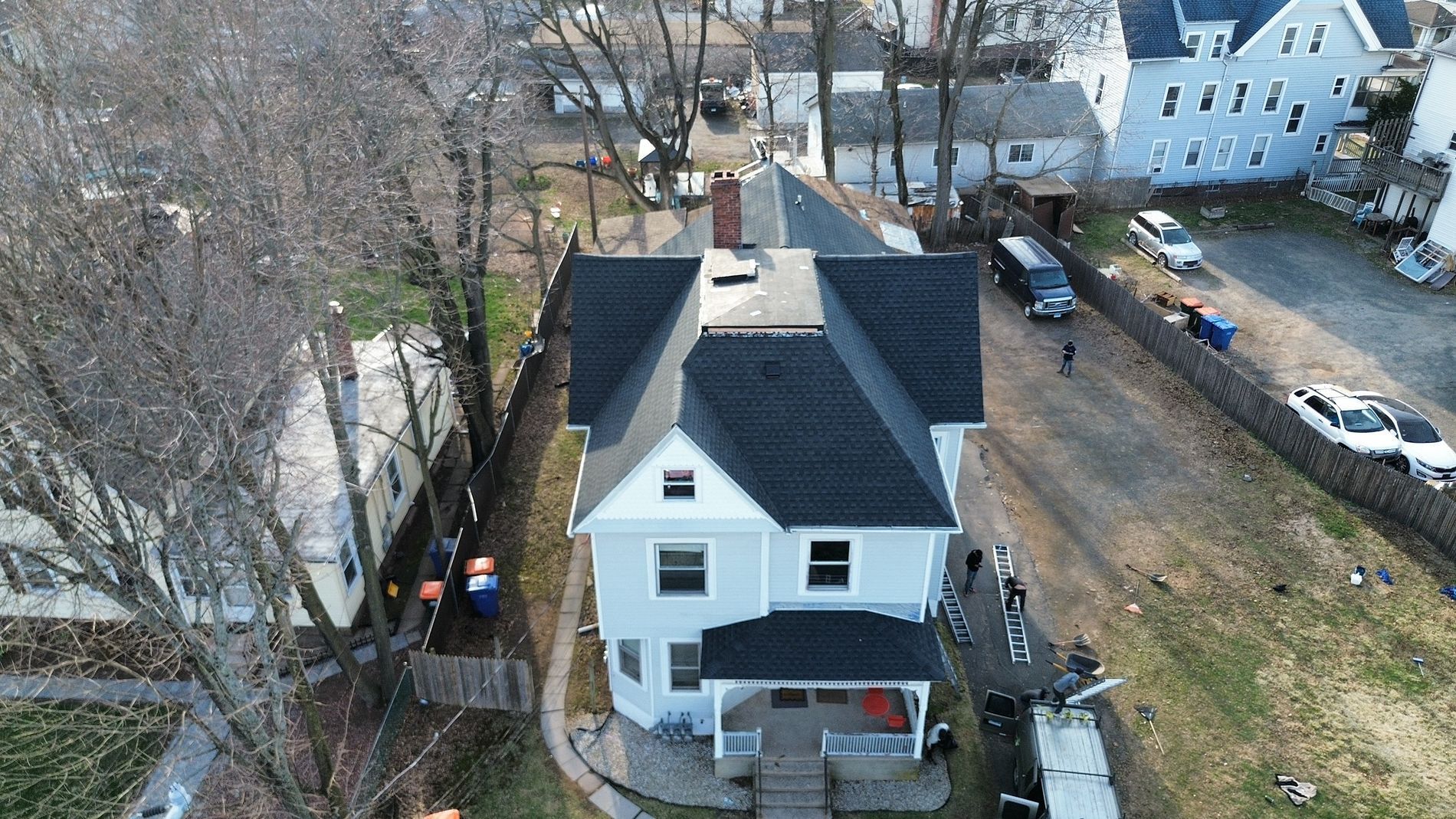 Aerial view of a white house with a dark roof, surrounded by trees and neighboring homes.