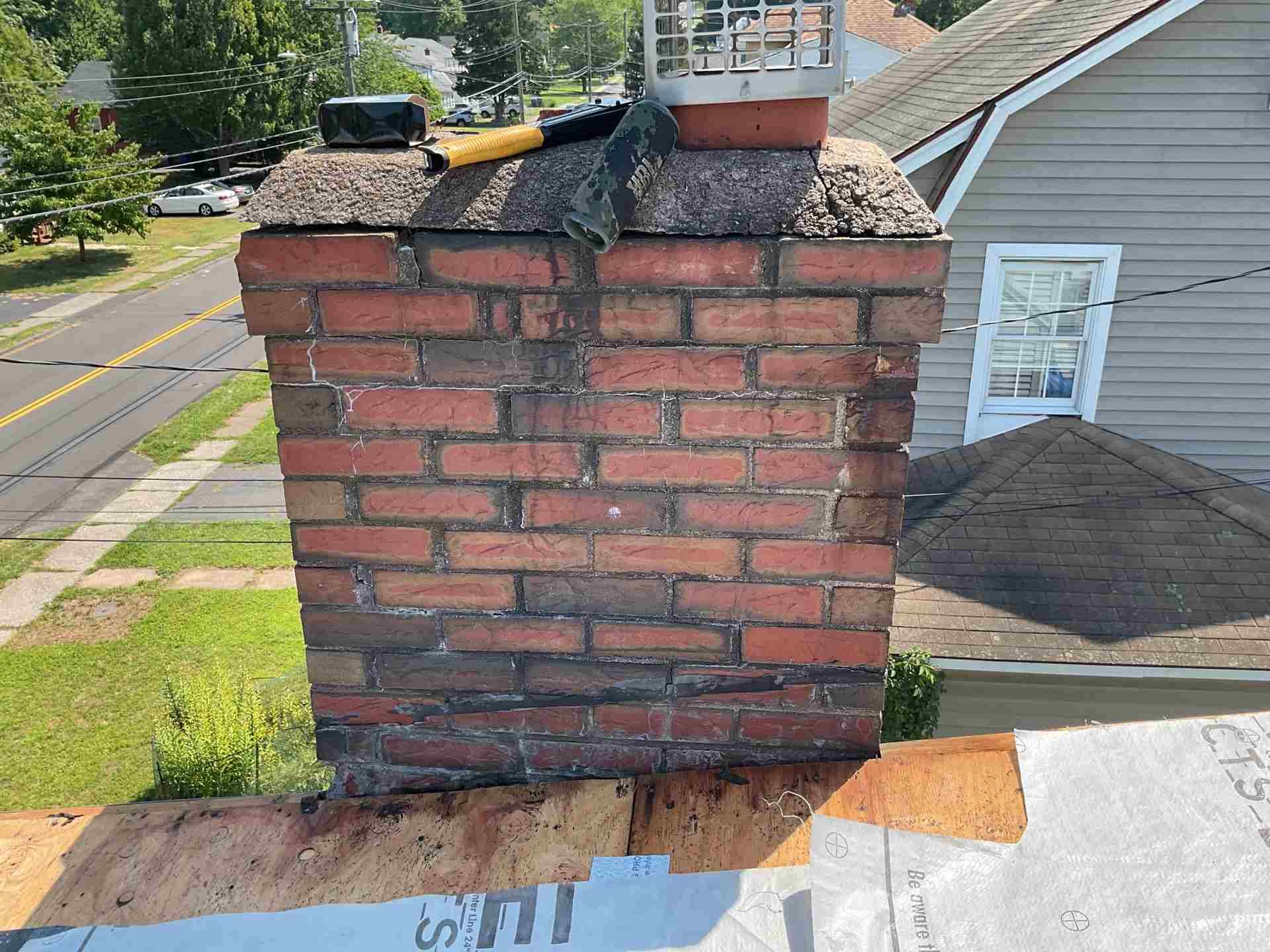 Brick chimney on a roof with damaged flashing and a black roof vent, viewed from above.