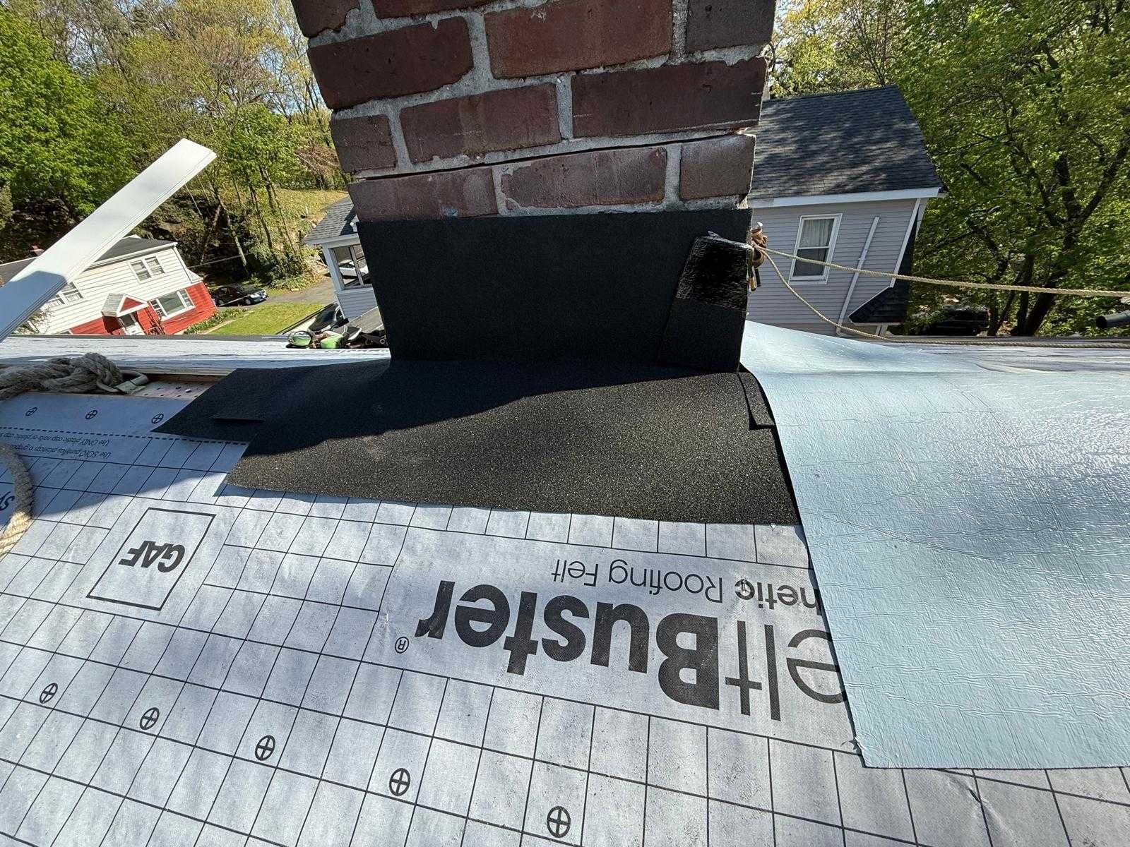Roofing underlayment installed around a brick chimney on a shingled roof