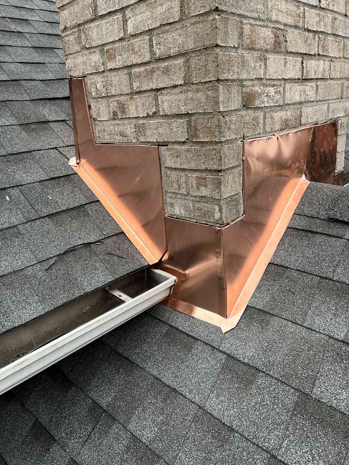 Copper roof flashing at a brick chimney where two shingle roofs meet