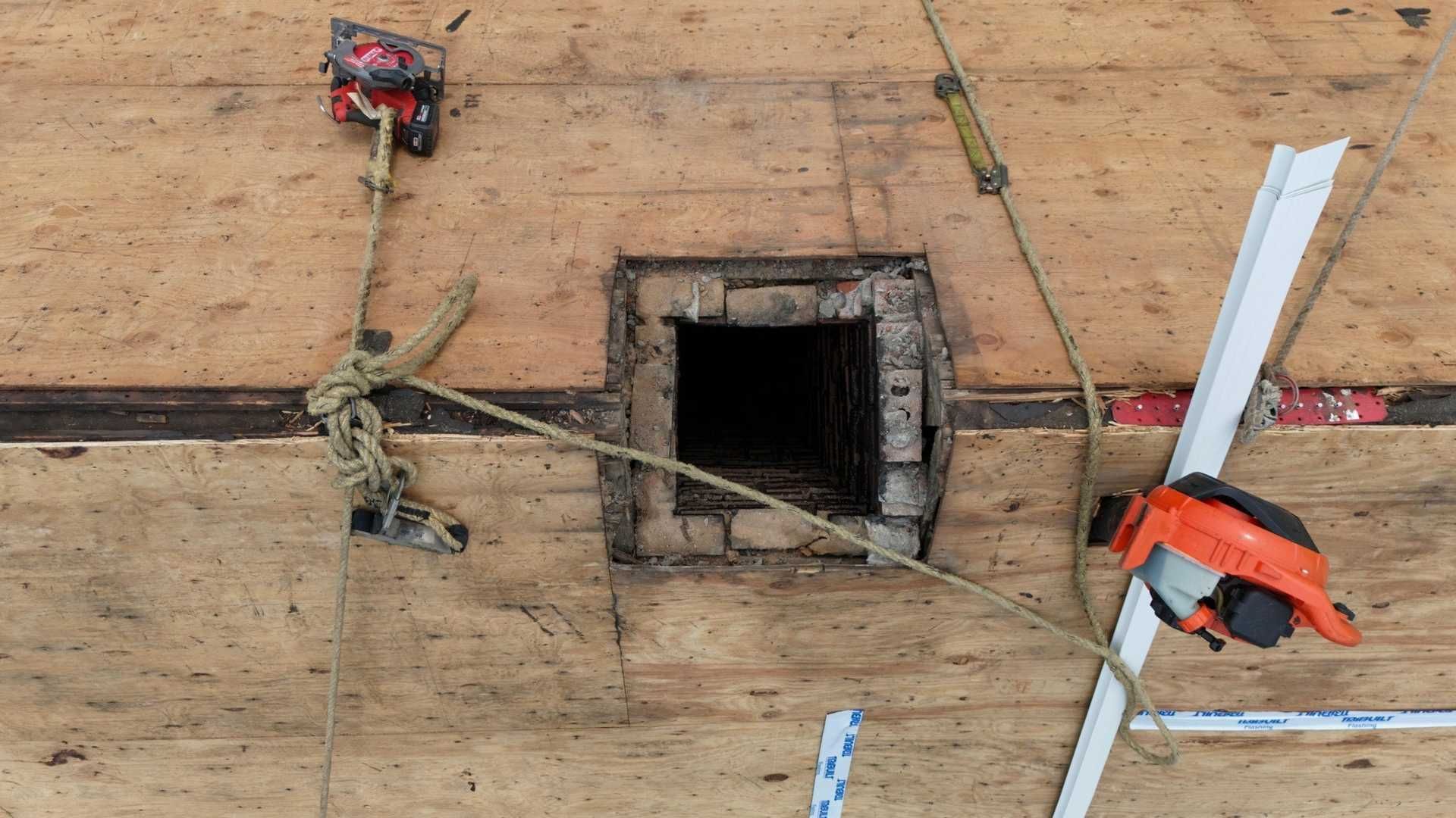 Overhead view of a plywood floor with a square cutout, rope, and tools around it