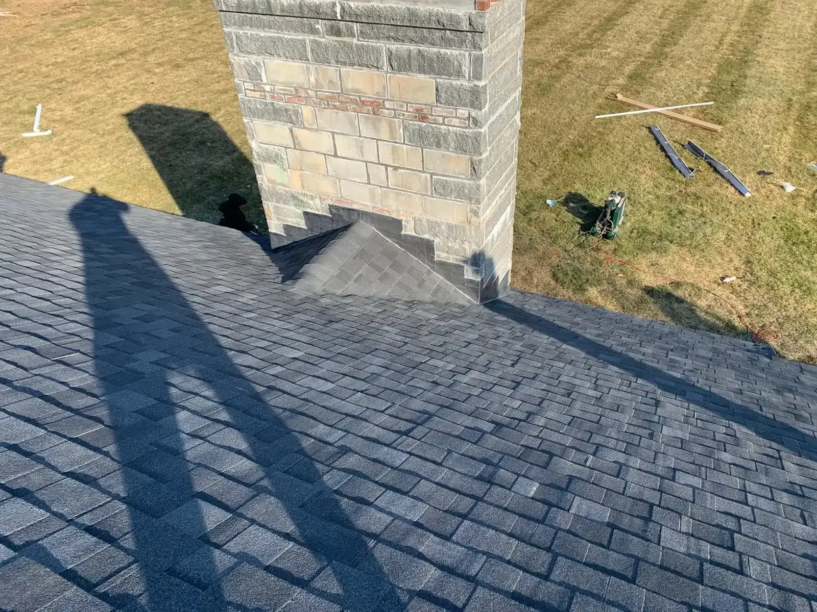 Shingled roof around a brick chimney, with long shadows on a sunny day.