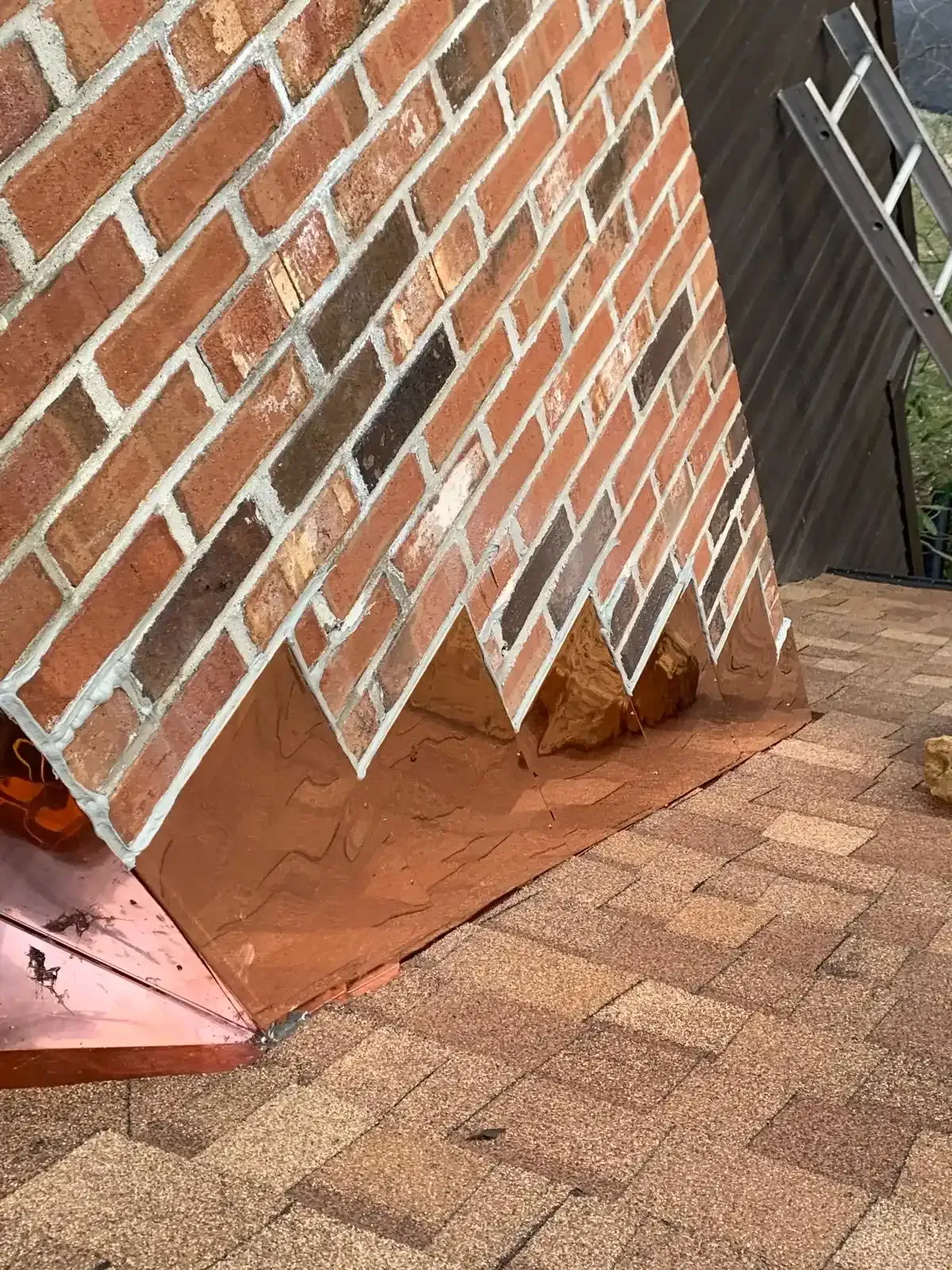 Brick wall with damaged lower edge and loose bricks beside a shingled roof.