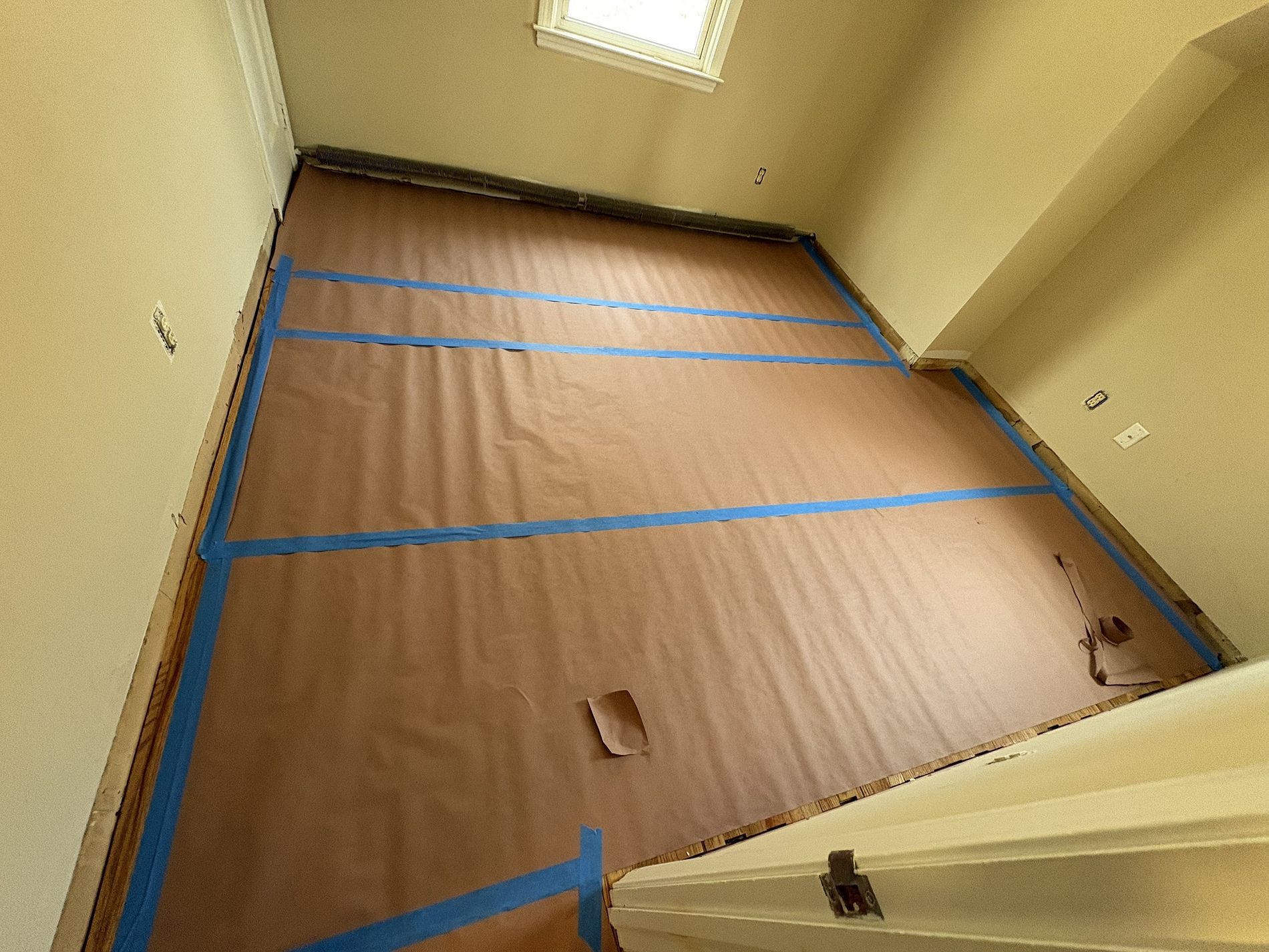 Empty room with brown floor paper taped down and blue painter’s tape around the edges.
