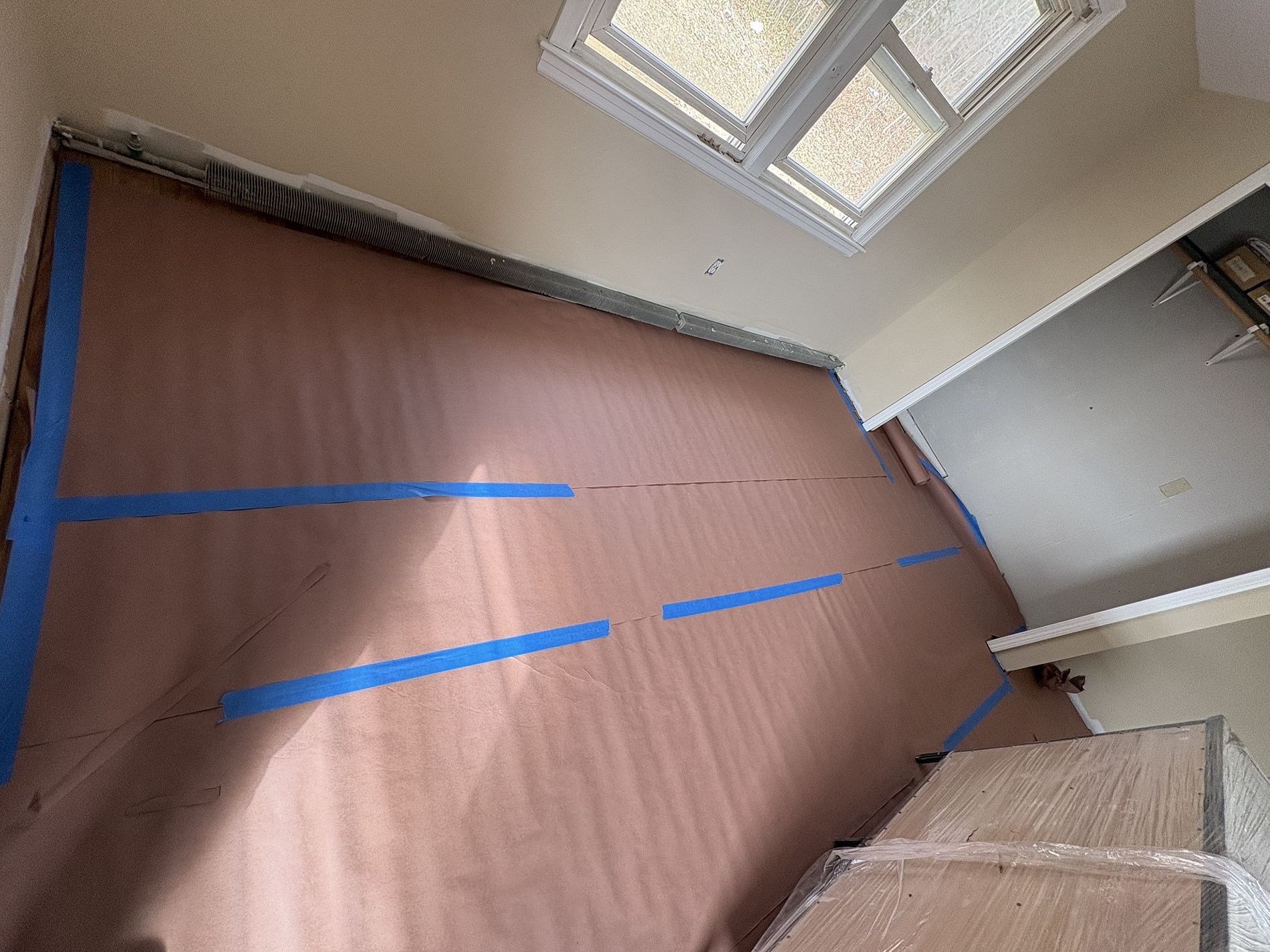 Empty room with brown floor covering, blue tape lines, and a skylight window above.