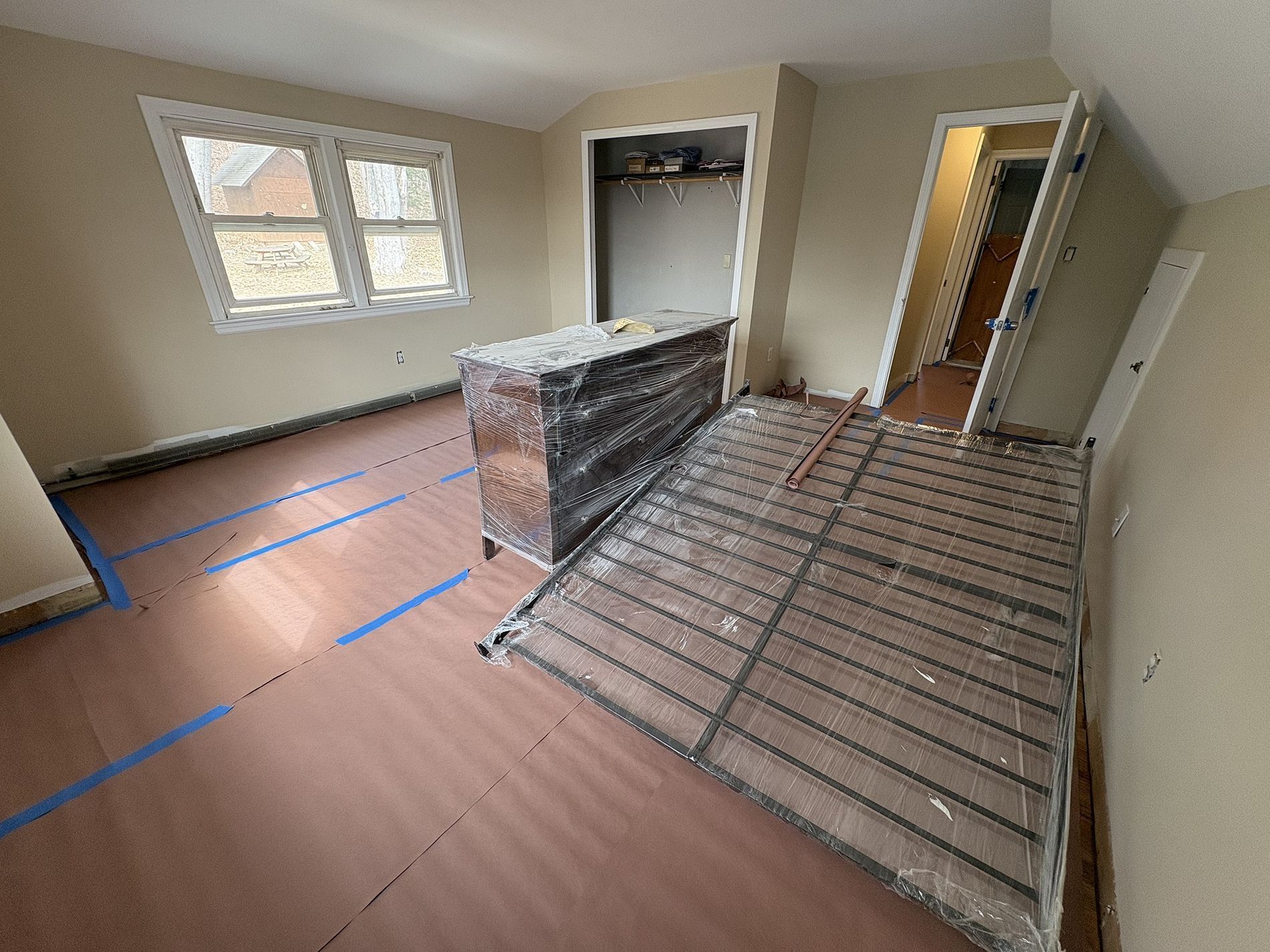 Empty room under renovation with taped floor, window, brick half-wall, and exposed subfloor boards