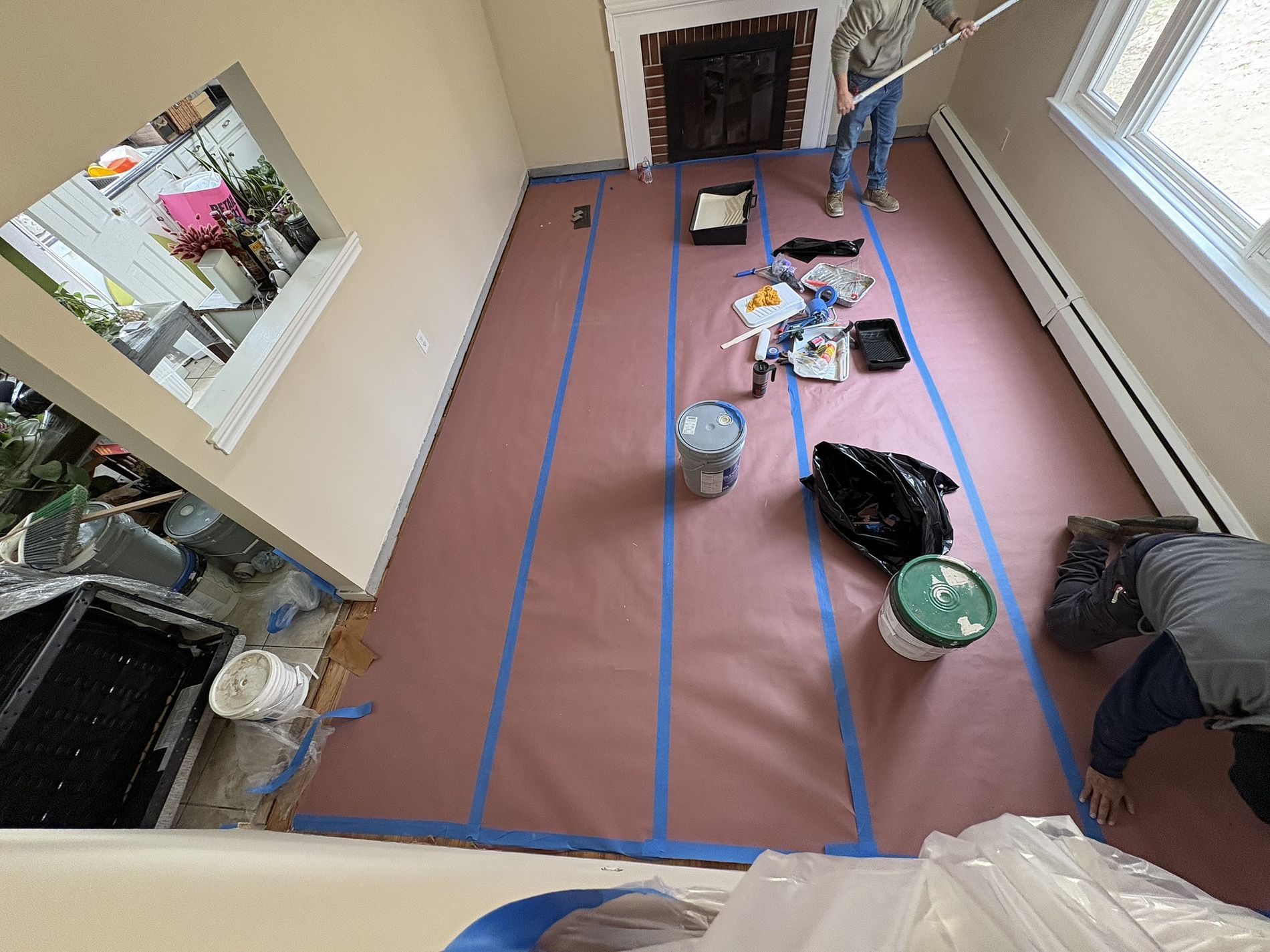 Room under renovation with pink floor covering, blue tape, tools, and a person near the window.