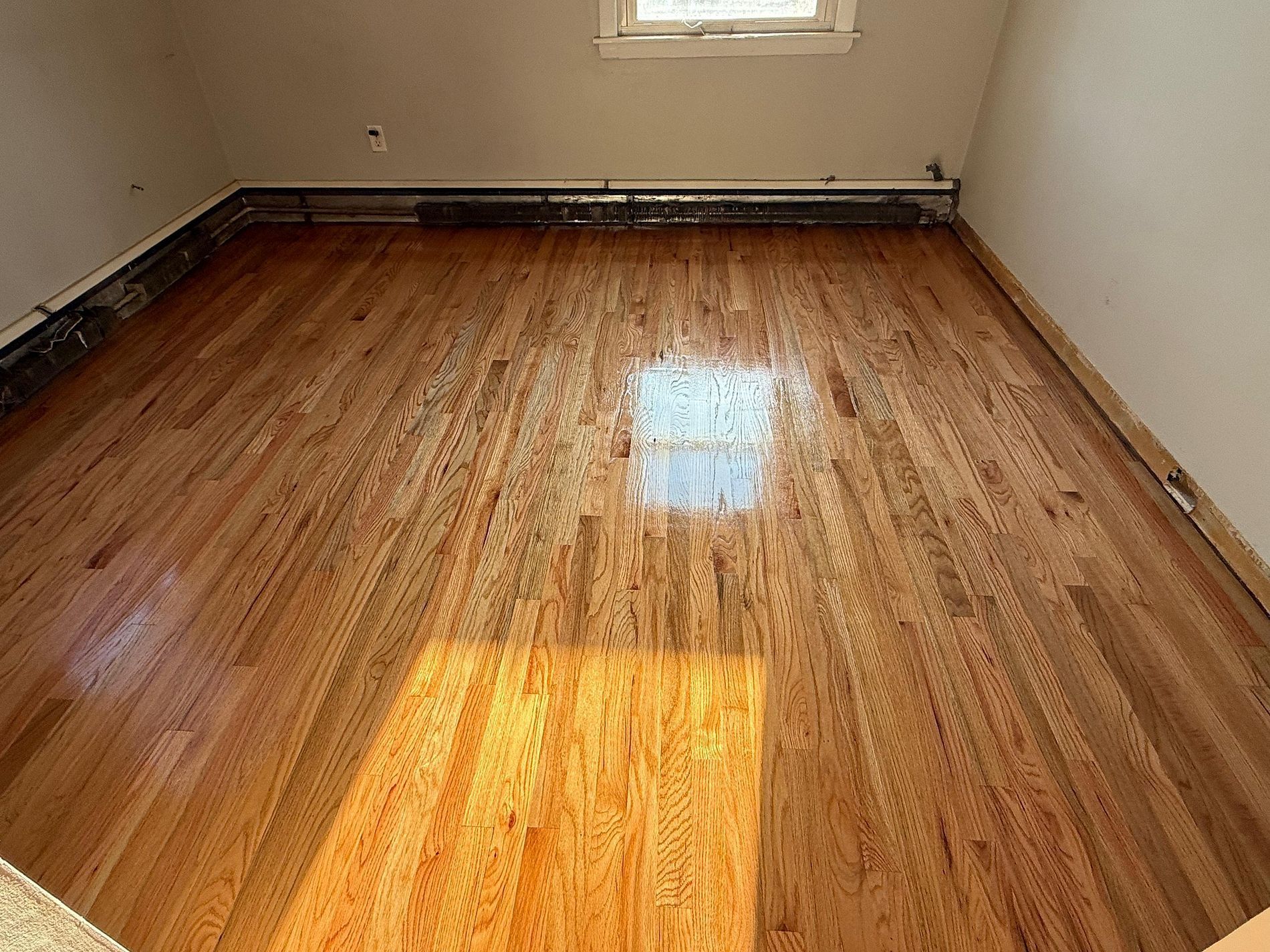 Empty room with hardwood floor and a small window casting sunlight on the floor