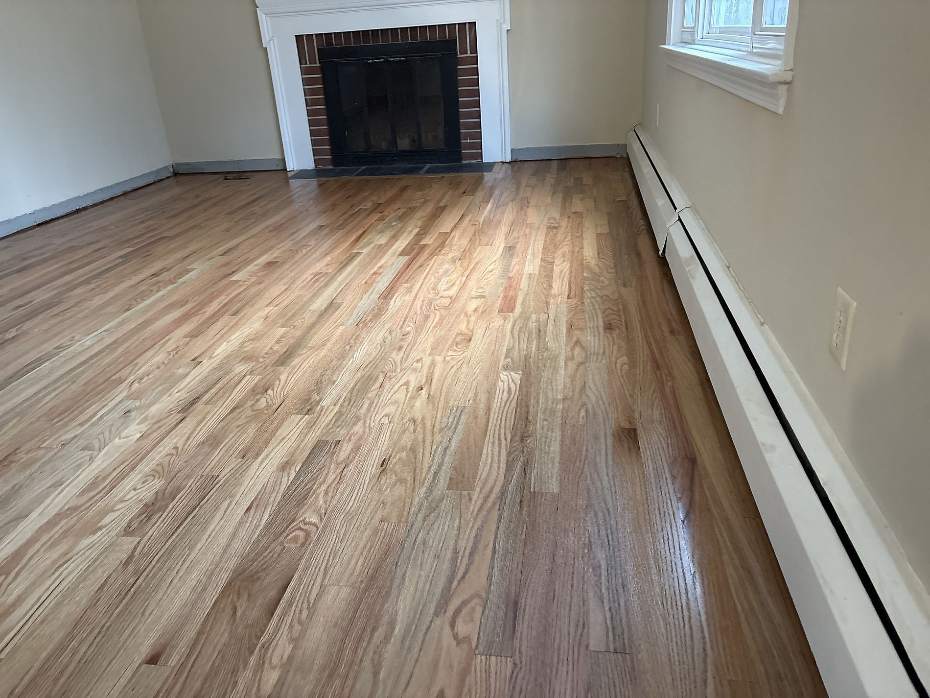 Empty room with wood floors, white walls, a fireplace, and a window along the right side.