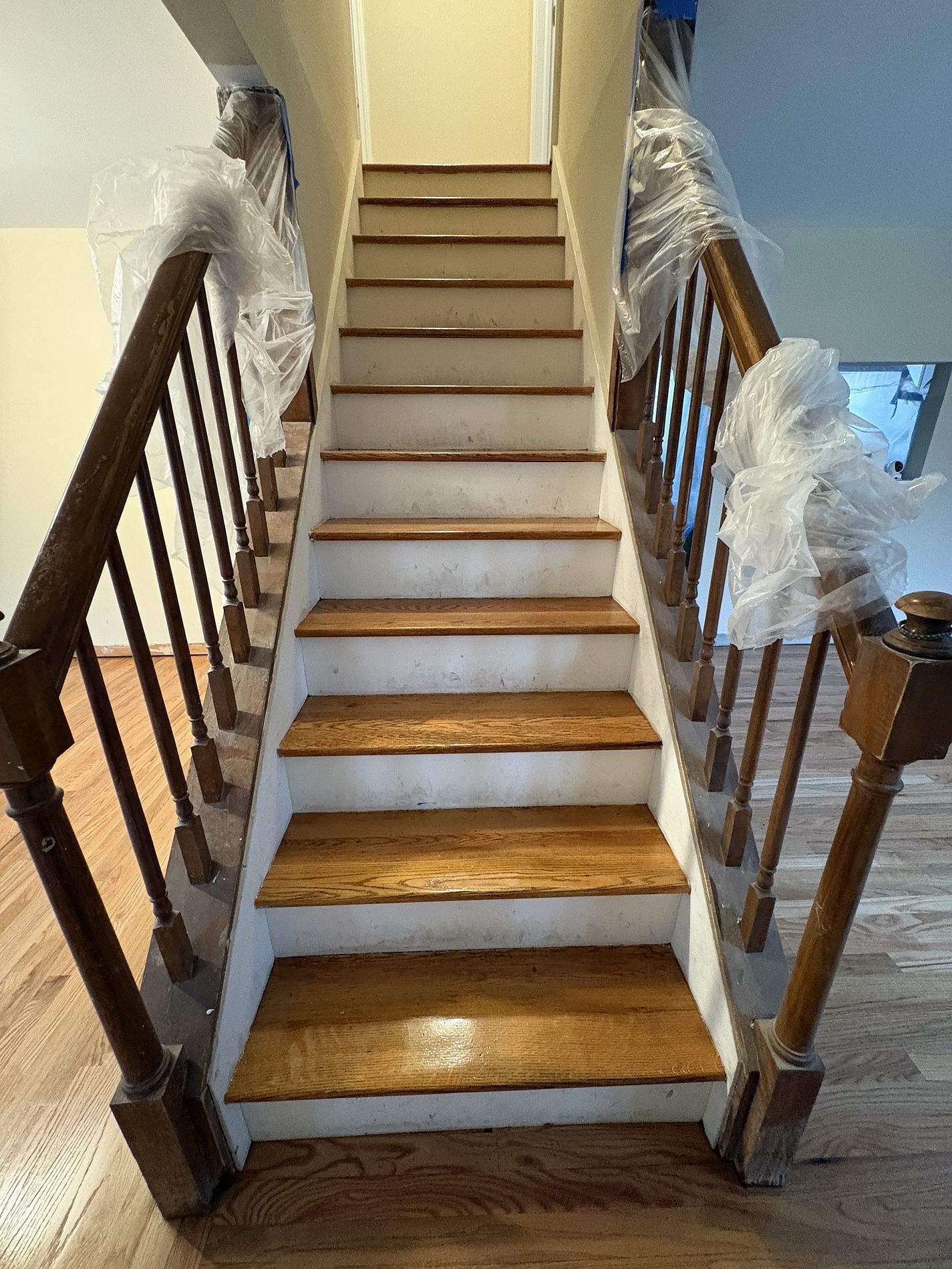 Staircase under renovation with plastic-wrapped banisters and unfinished wooden steps