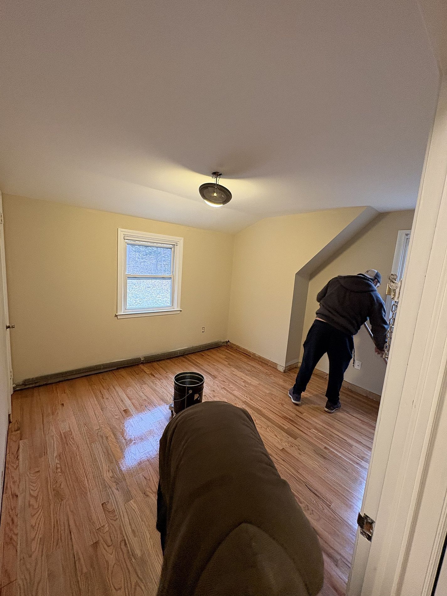 Empty beige room with hardwood floor; one person stands by the doorway looking out.