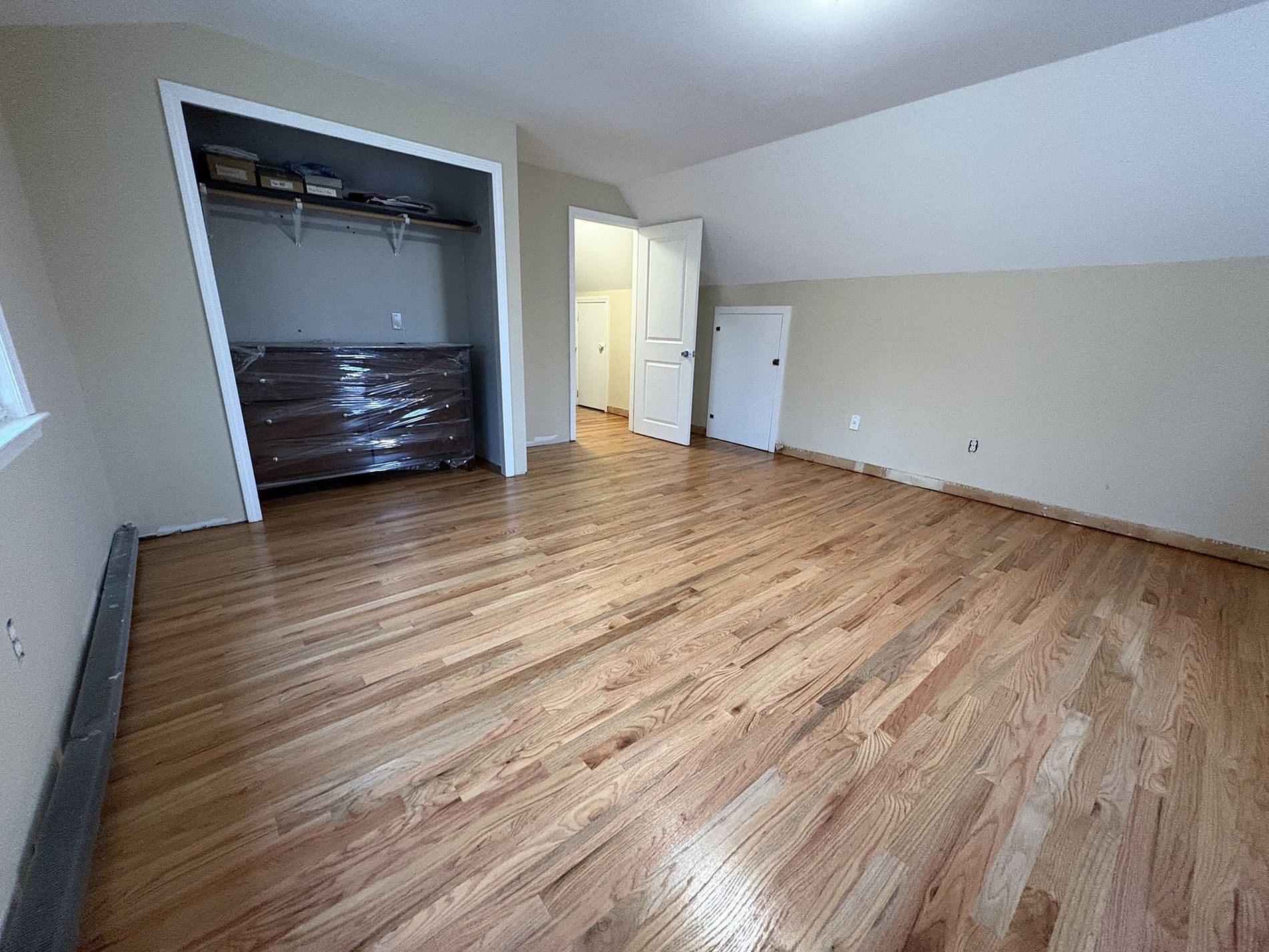 Empty bedroom with wood floors, open closet, and white walls under a sloped ceiling