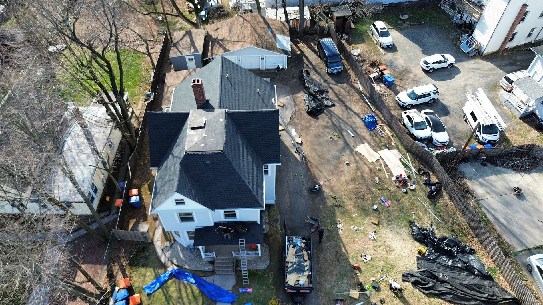 Aerial view of a damaged white house and yard with debris, fallen trees, and cleanup equipment after storm damage