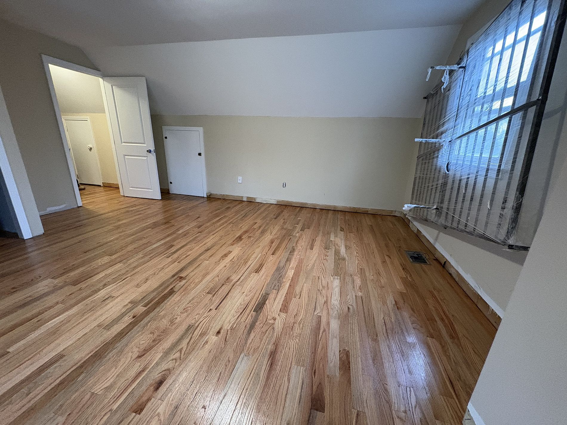Empty room with wood floors, beige walls, and large windows with vertical blinds.