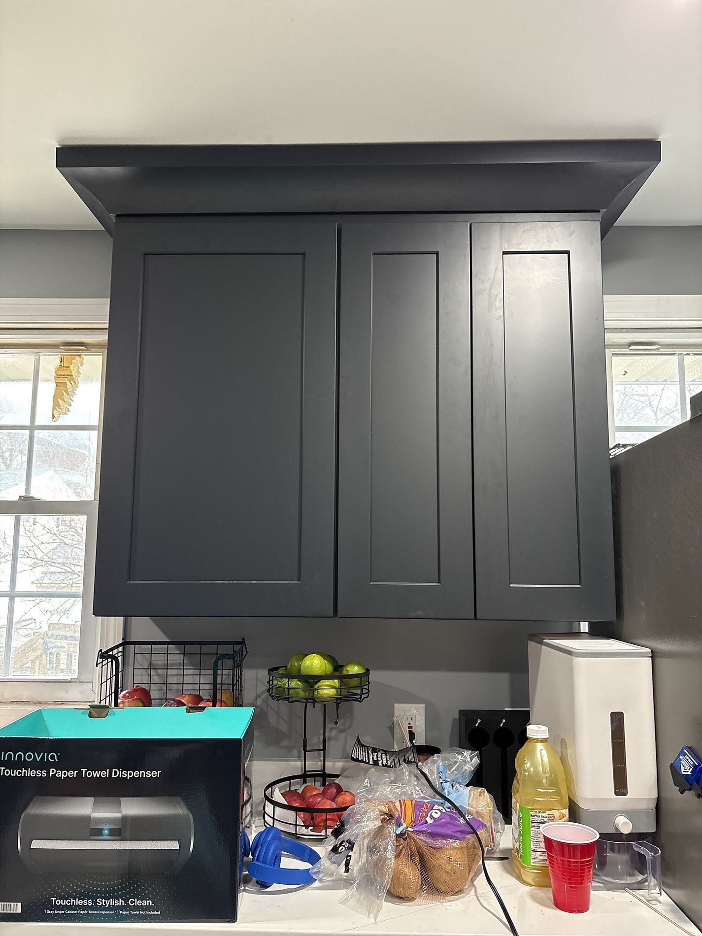 Kitchen cabinets above a counter with a toaster oven, fruit bowl, bread, and paper towel roll