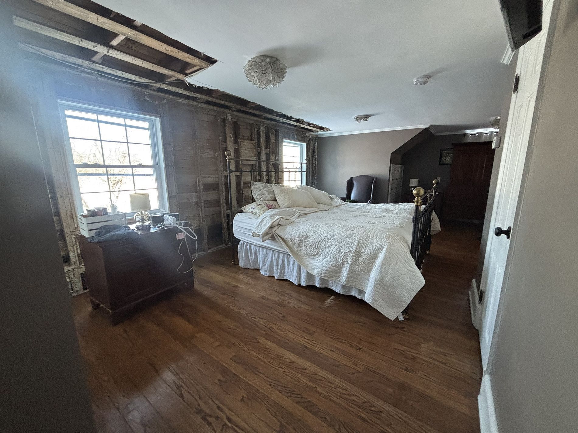 Spacious bedroom with unmade bed, wooden floor, and large windows letting in daylight