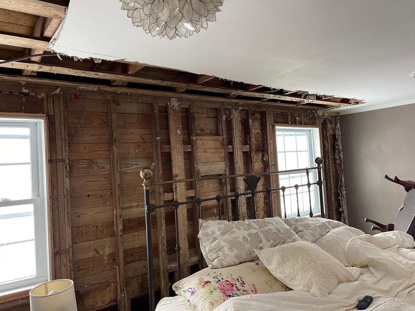 Bedroom under renovation with exposed walls, damaged ceiling, and a bed with white bedding in the foreground