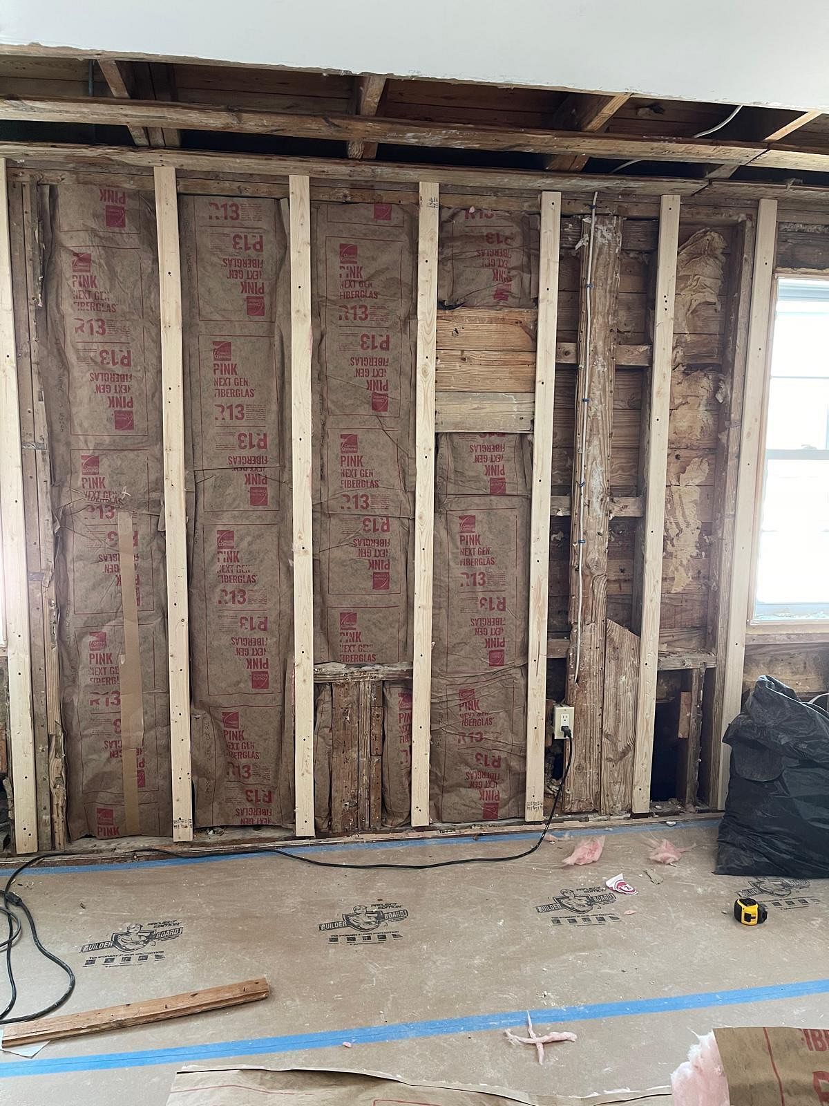 Exposed wall framing in an unfinished room with insulation, exposed joists, and debris on the floor