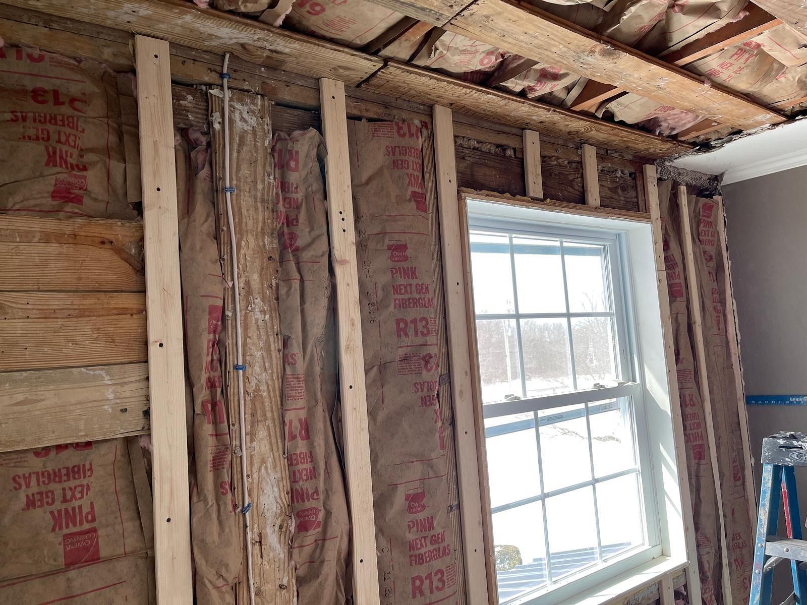 Exposed wall framing and insulation around a window in a room under renovation