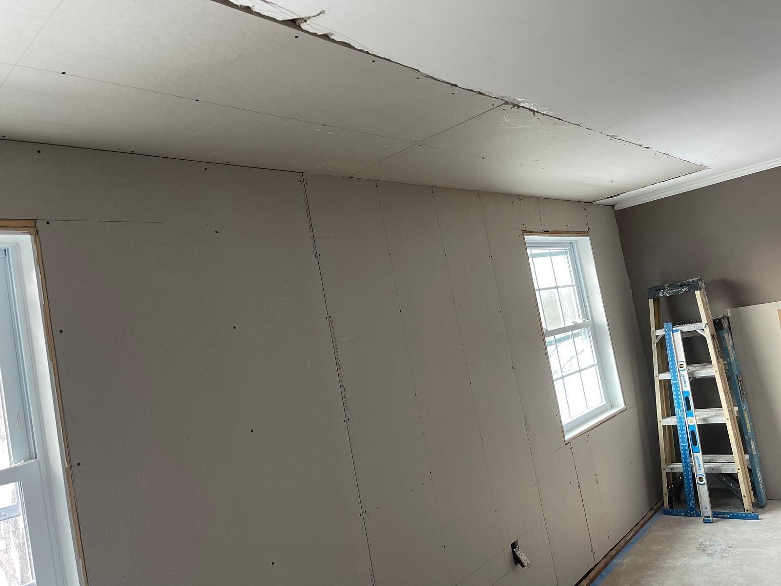 Partially finished room with gray walls, white ceiling, windows, and a ladder near the corner
