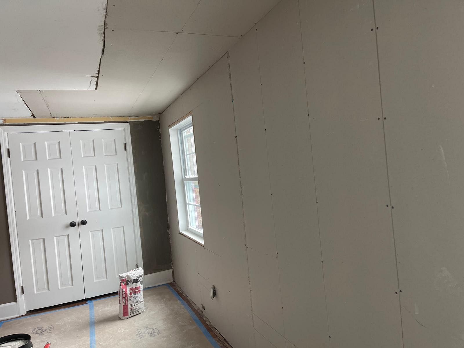 Unfinished room with drywall, white double doors, a window, and a bucket on the floor.