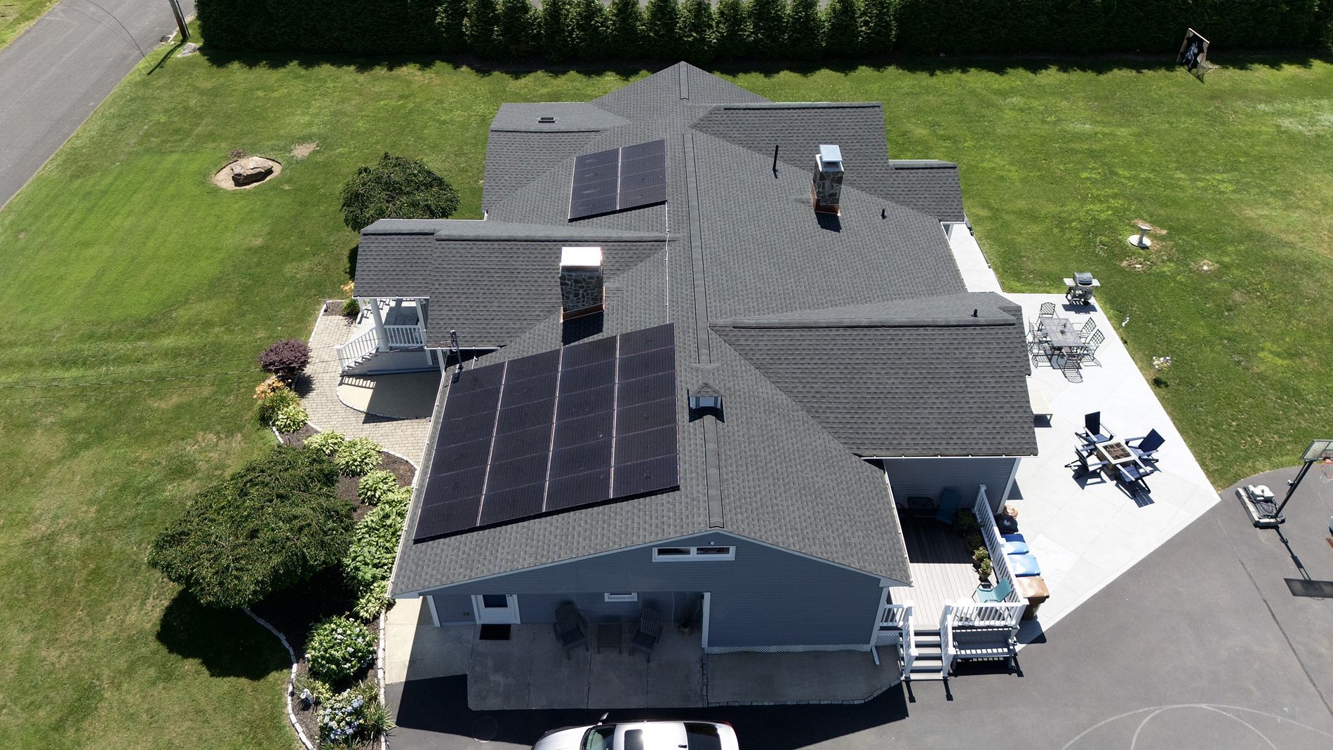 Aerial view of a house with dark solar panels on the roof and a driveway beside a green lawn.