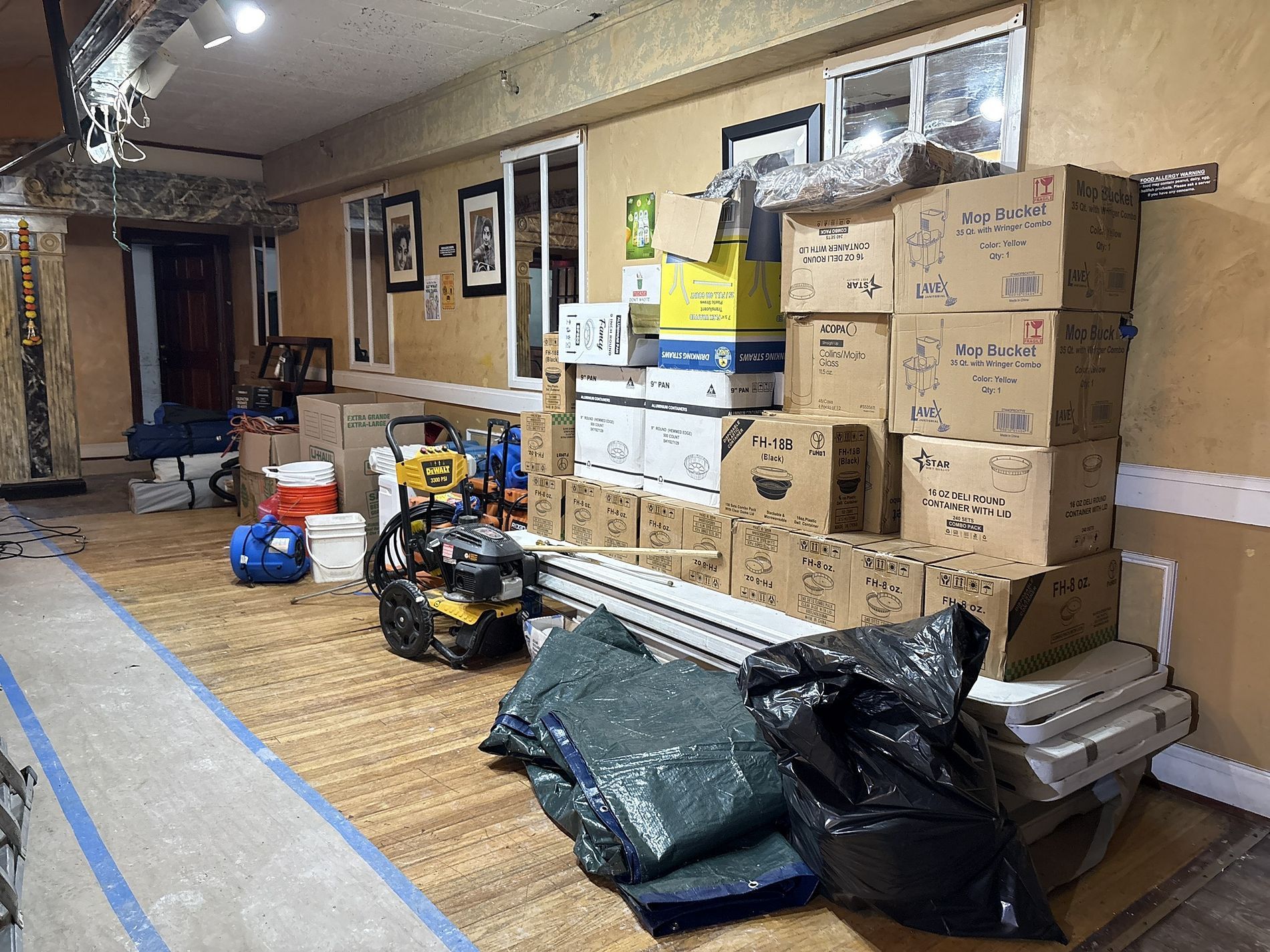 Hallway with stacked cardboard boxes, supplies, and equipment covered with tarps in a storage-like space