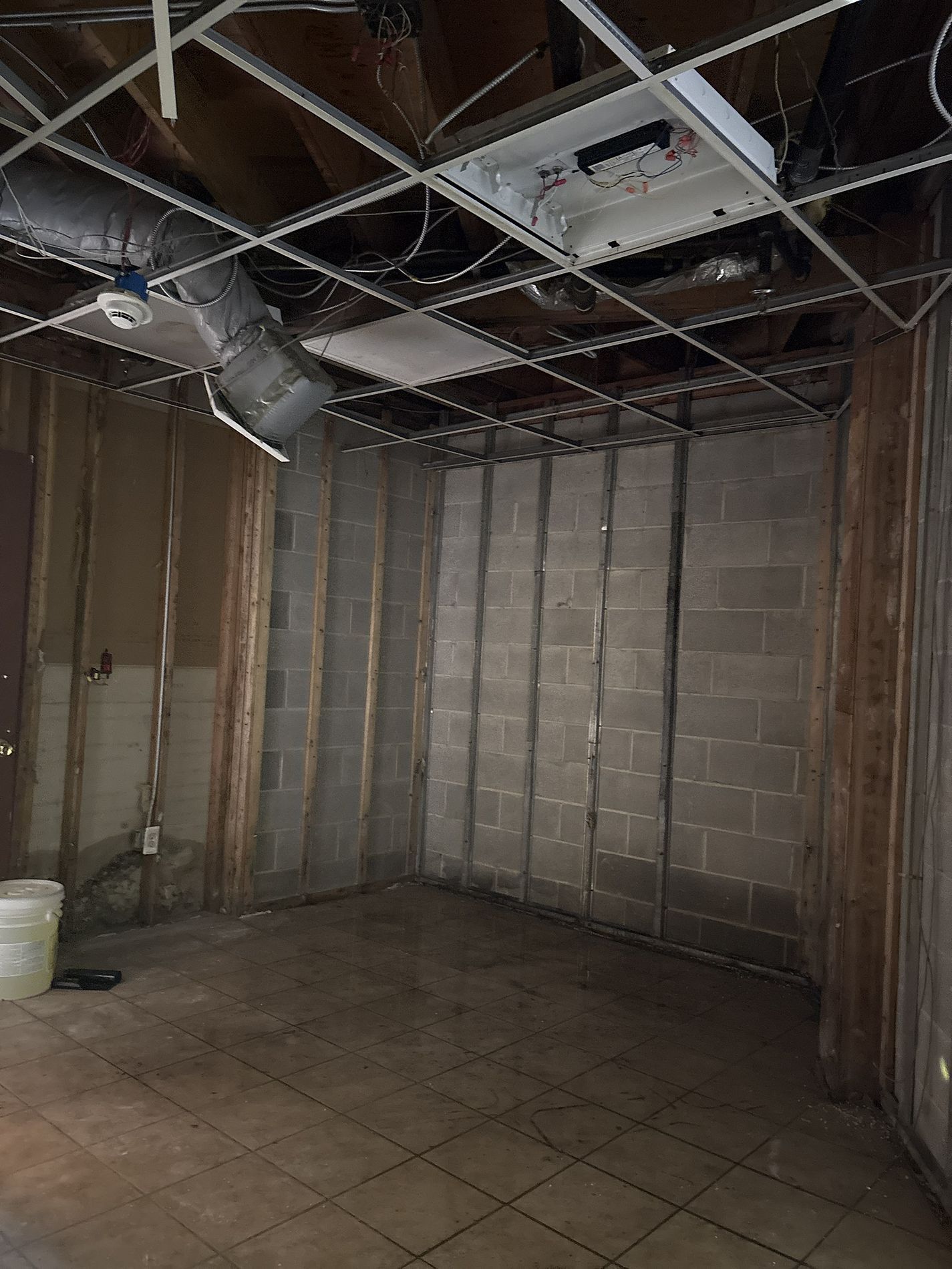 Bare unfinished basement room with exposed ceiling pipes, concrete block walls, and tiled floor