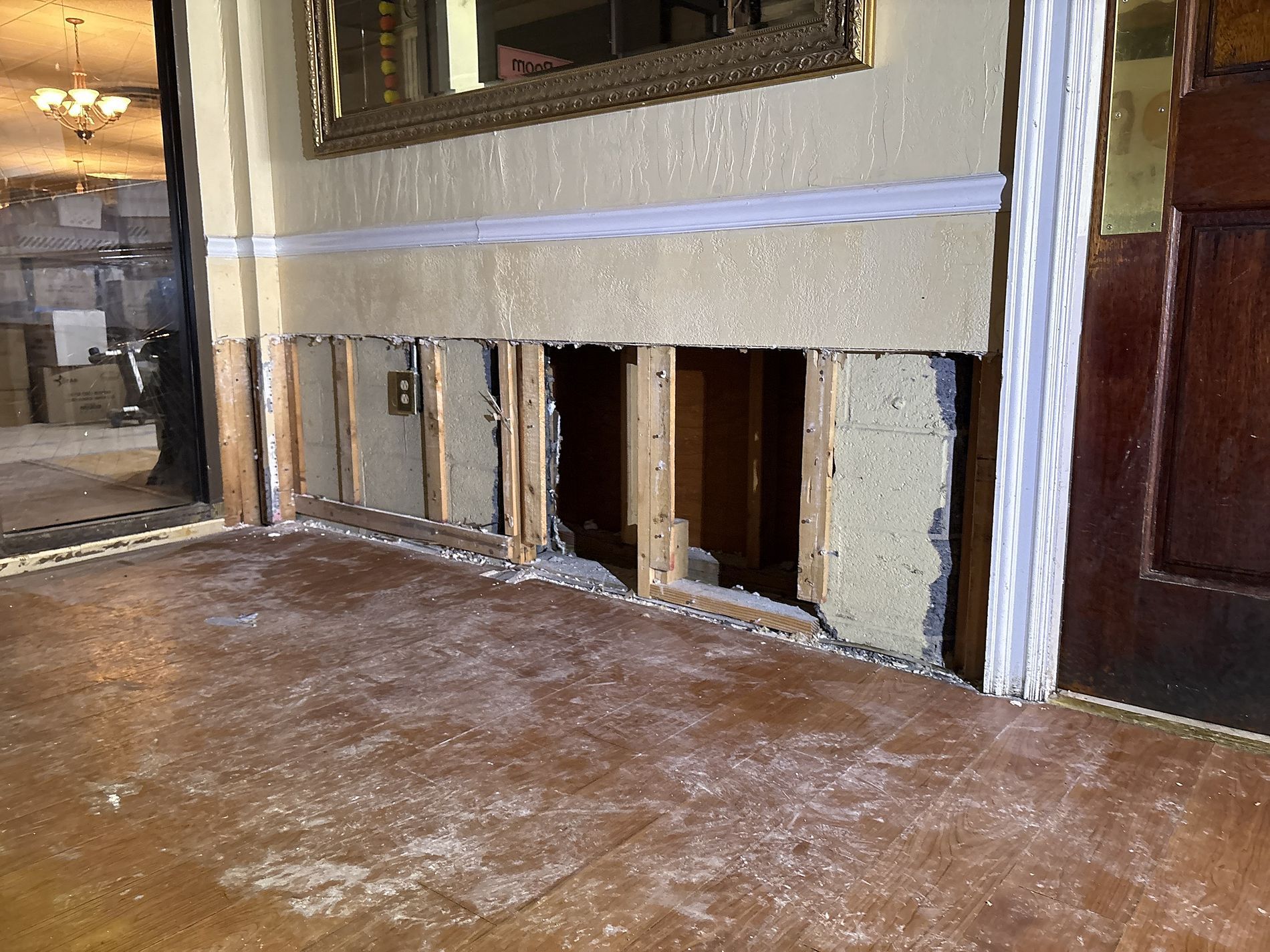 Damaged interior wall with exposed framing and debris on the floor in a partially demolished room