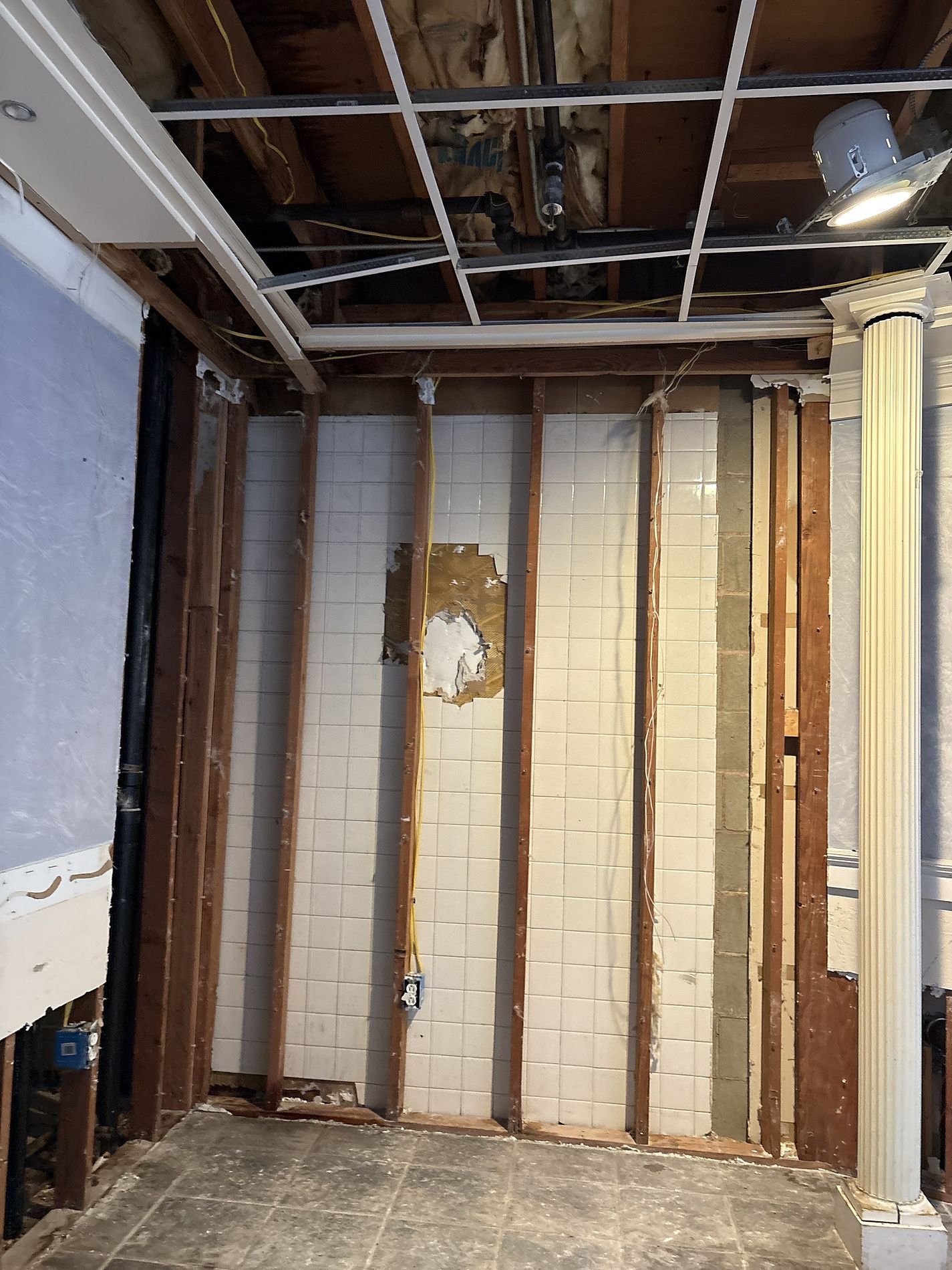 Damaged interior wall with exposed studs, drywall, insulation, and a partially removed ceiling.