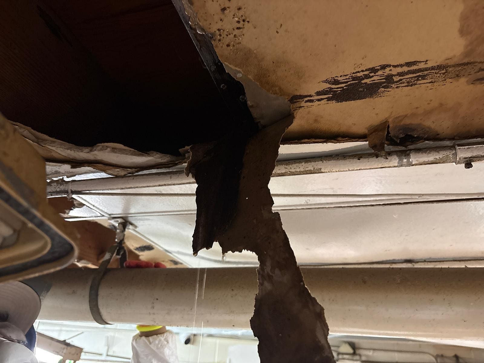Damaged ceiling with a large hole and hanging debris, exposing interior layers.