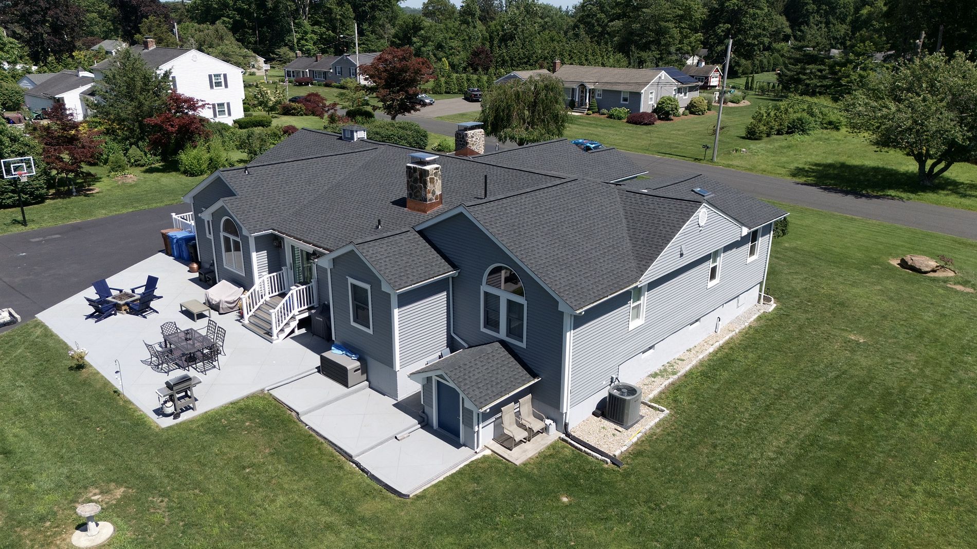 Aerial view of a gray suburban house with a large lawn and paved patio area.