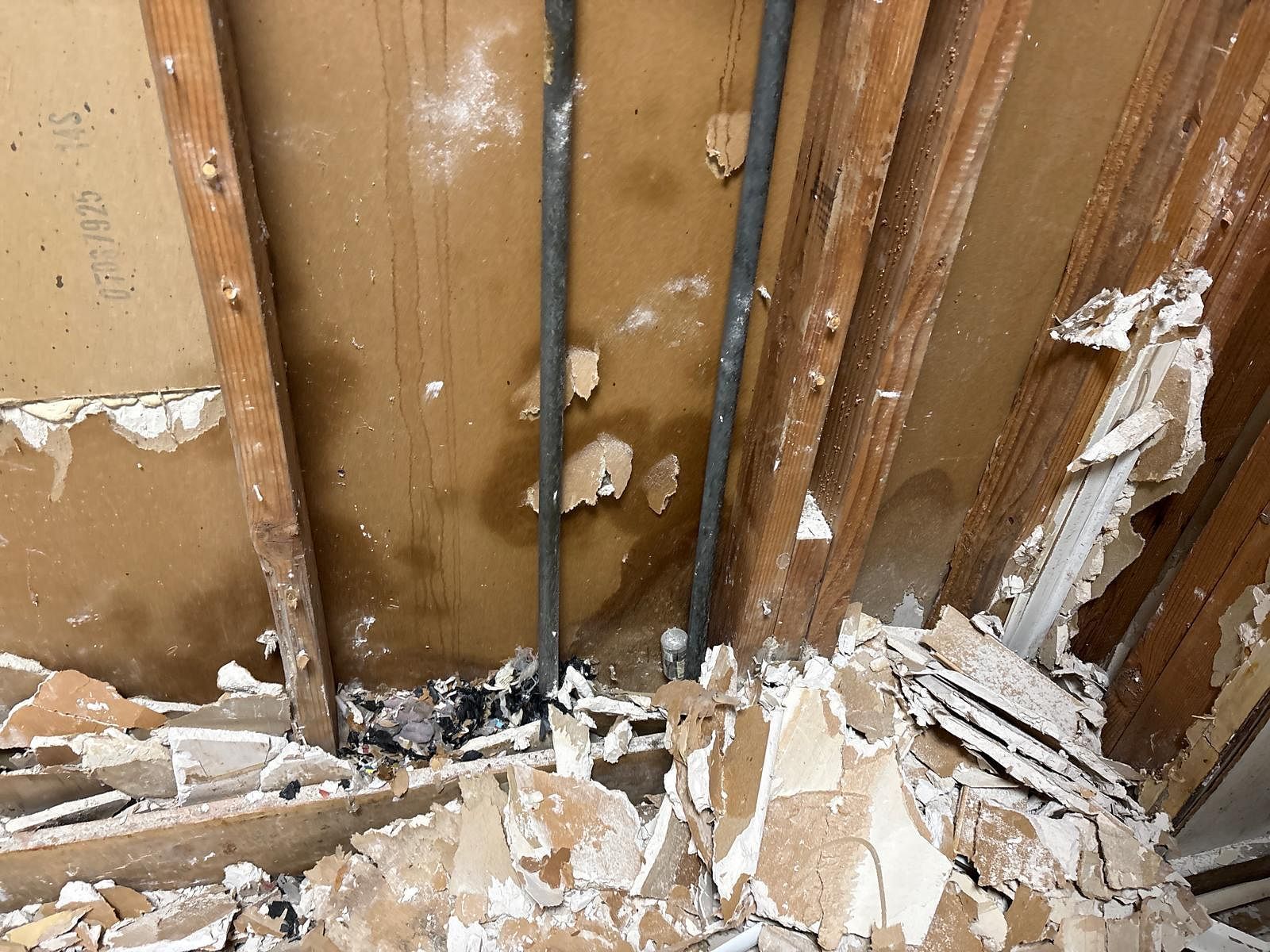 Damaged wall framing with exposed studs, peeling plaster, and debris on the floor