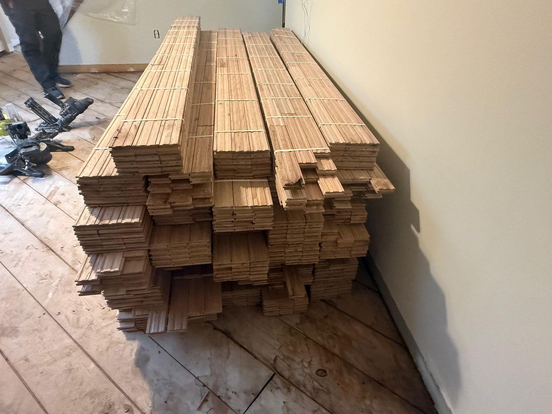 Stacked wooden planks on a tiled floor beside a wall, with tools and debris nearby.