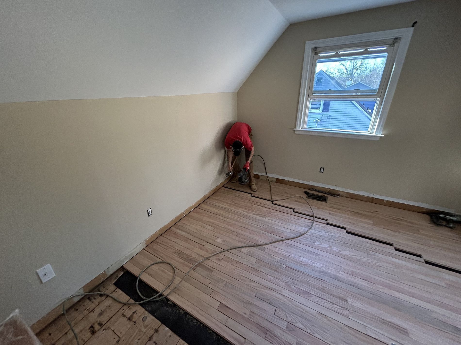 Person sanding a bare upstairs room floor near a window during renovation
