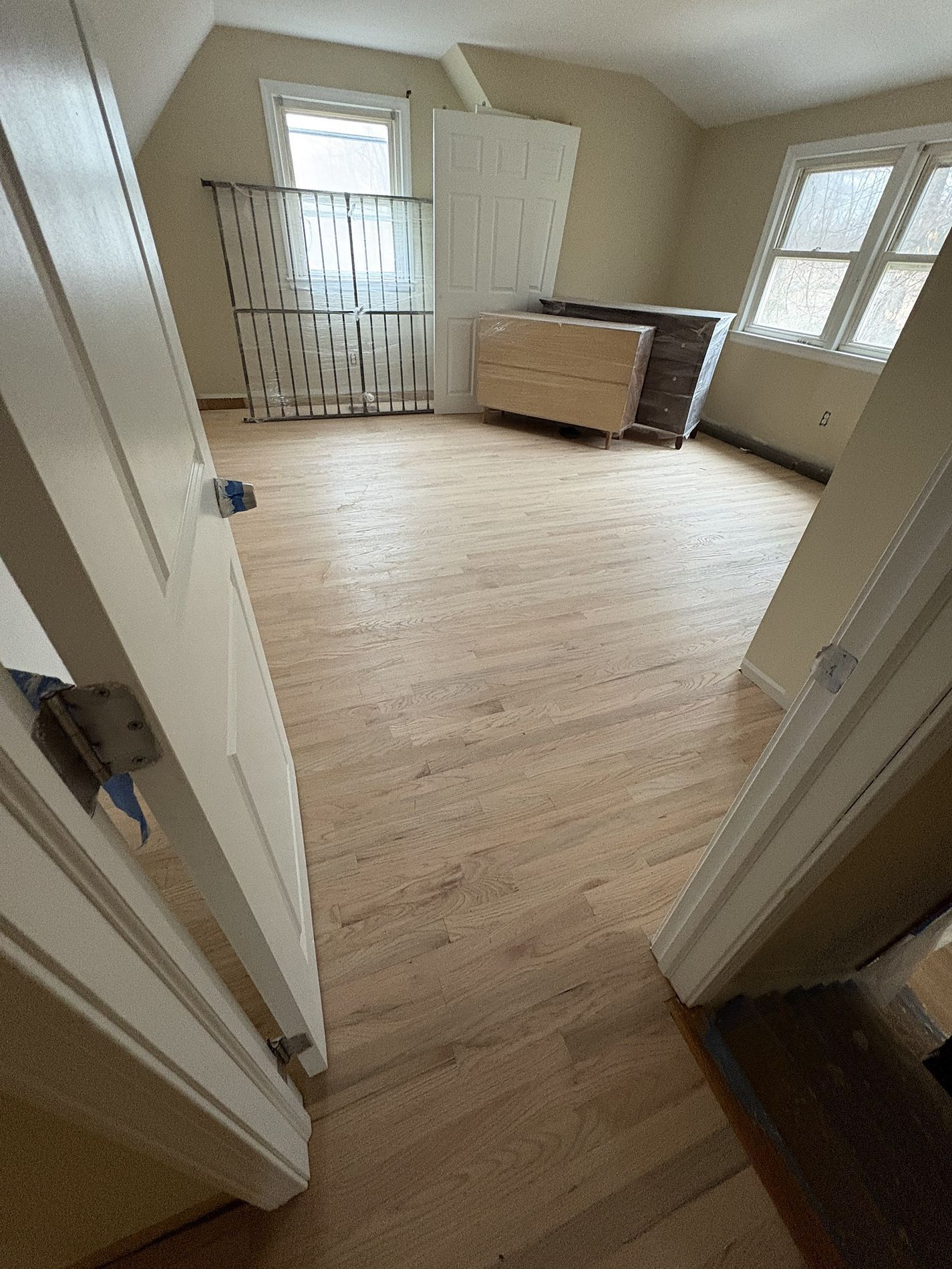 Empty beige bedroom with wood floors, twin doors, a dresser, and a window with curtains.