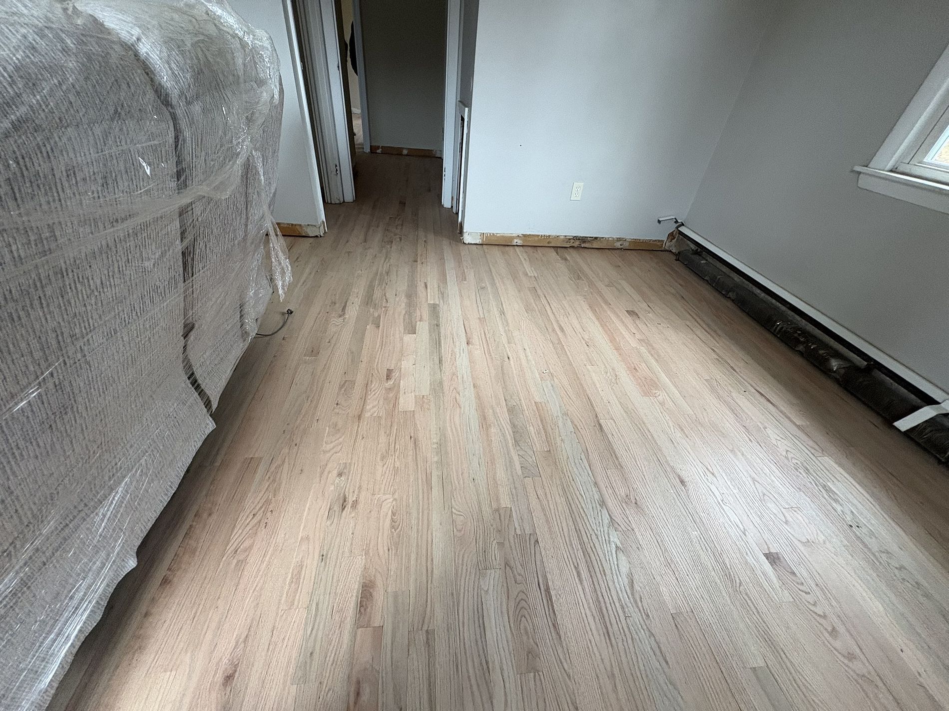 Empty room with light wood flooring, white walls, and a doorway at the far end