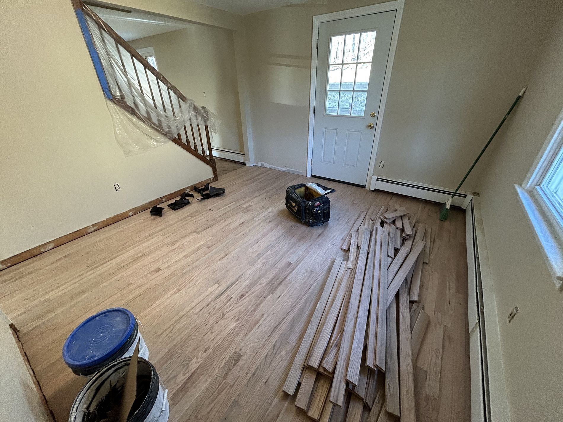 Partially renovated entry room with wood flooring, stairs, door, and stacked lumber on the floor