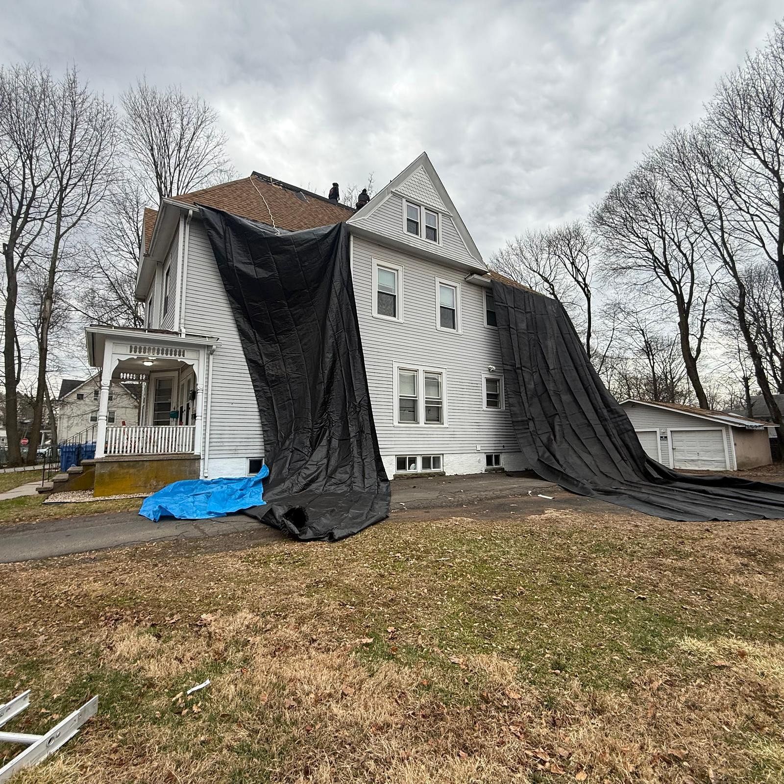 House covered in black tarps during roof repair, with bare trees and an overcast sky.
