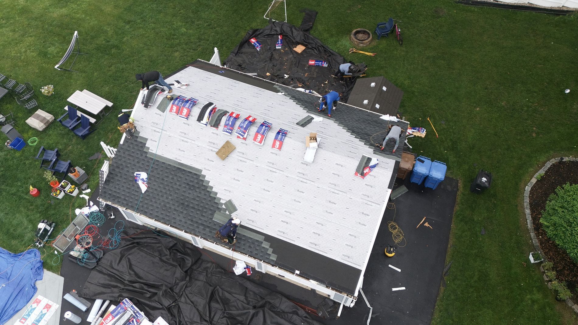 Aerial view of a white-roofed event tent with people and colorful items on a wet outdoor lawn
