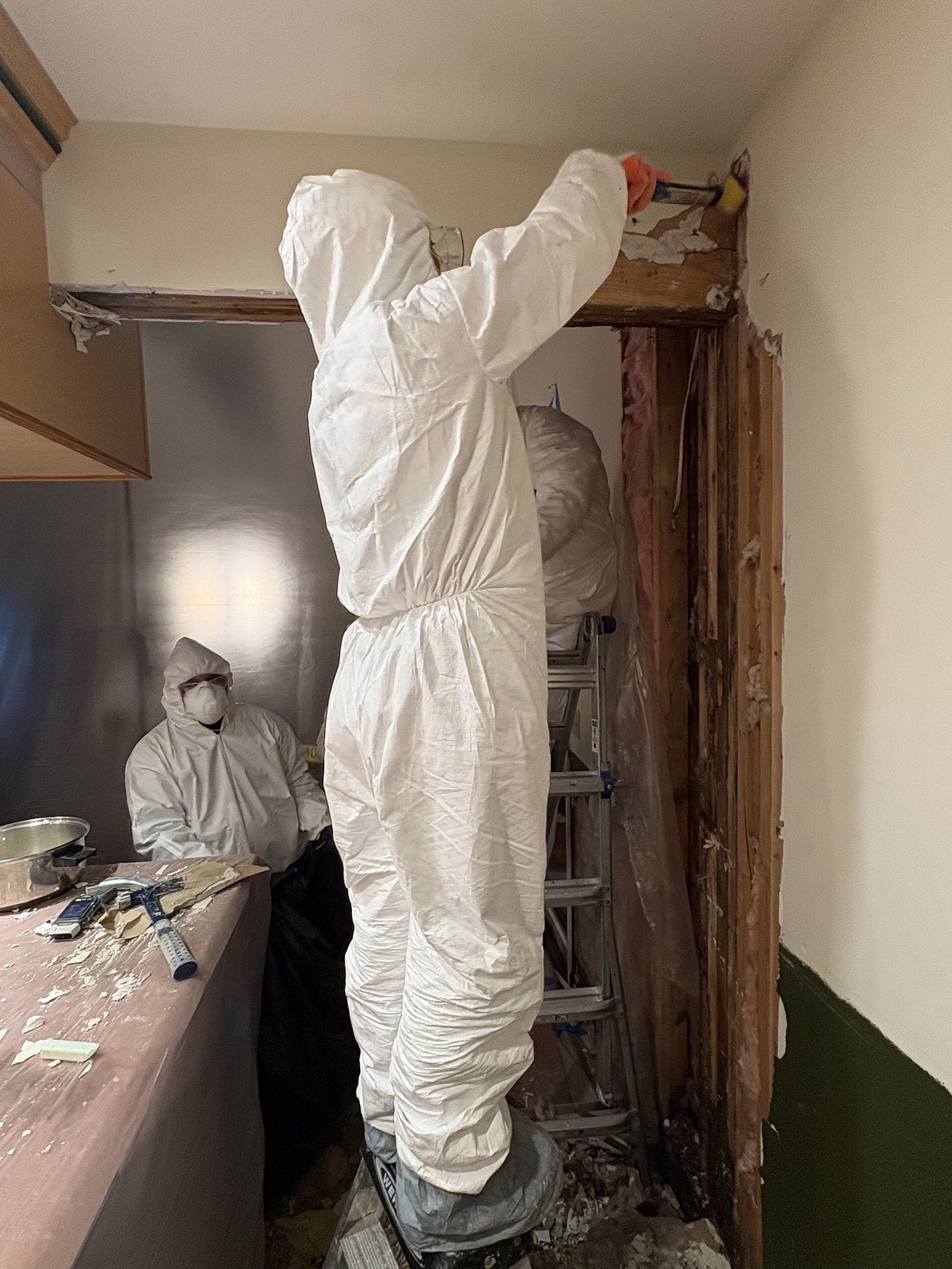 Workers in white protective suits painting and repairing a room doorway