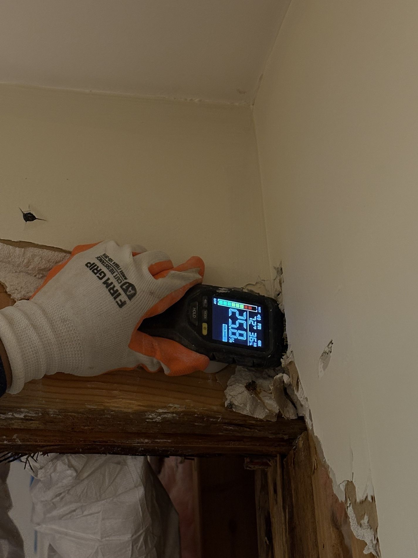 Gloved hand holding a digital thermometer to a bed frame in a damaged room