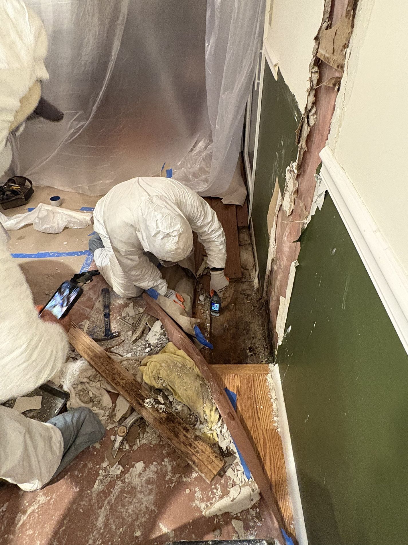 Workers in white suits removing debris and damaged drywall in a damaged room
